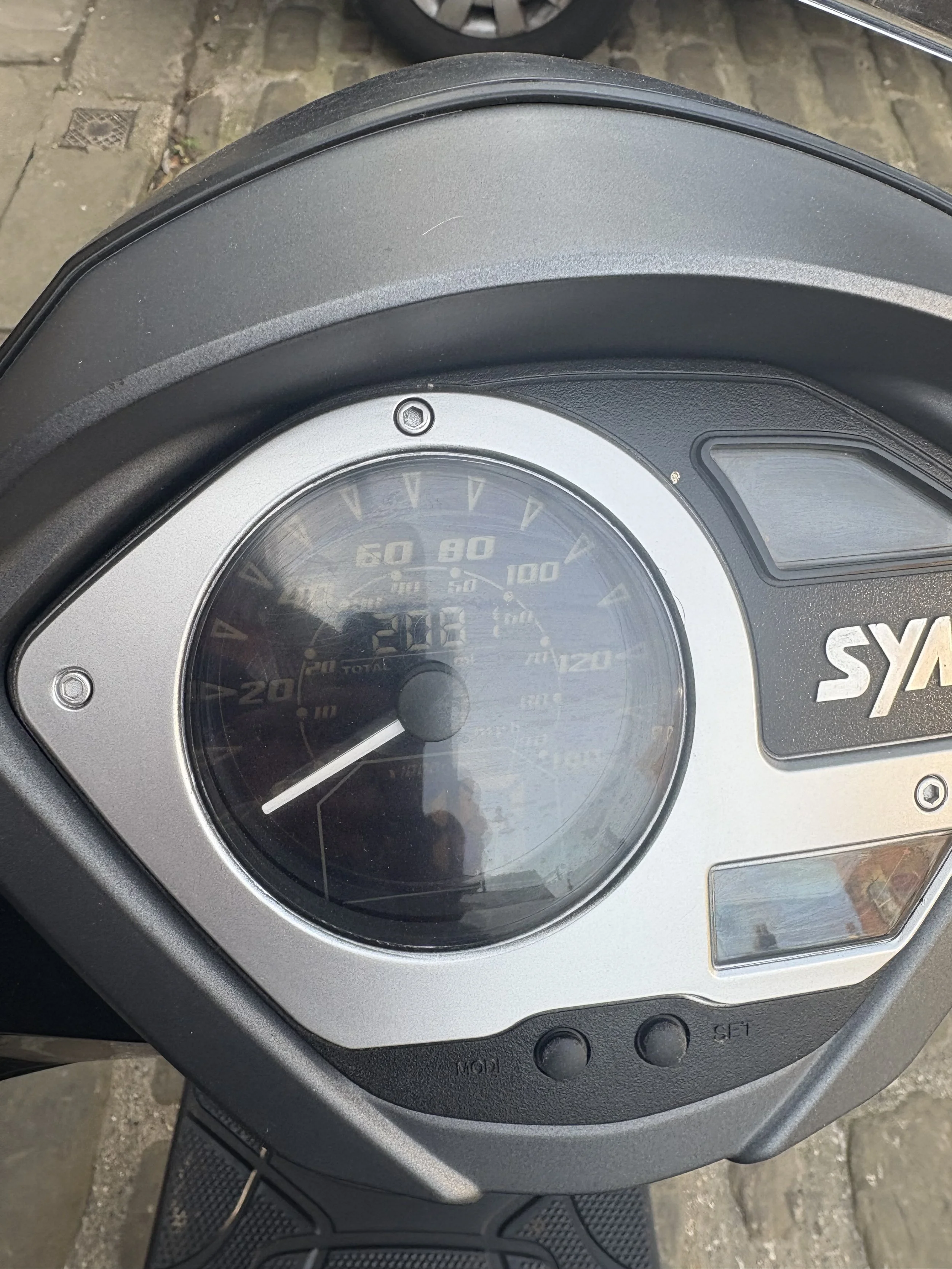 Close-up image of a motorcycle's speedometer, showing a speed of around 25 miles per hour, with other gauges faintly visible behind the glass cover.