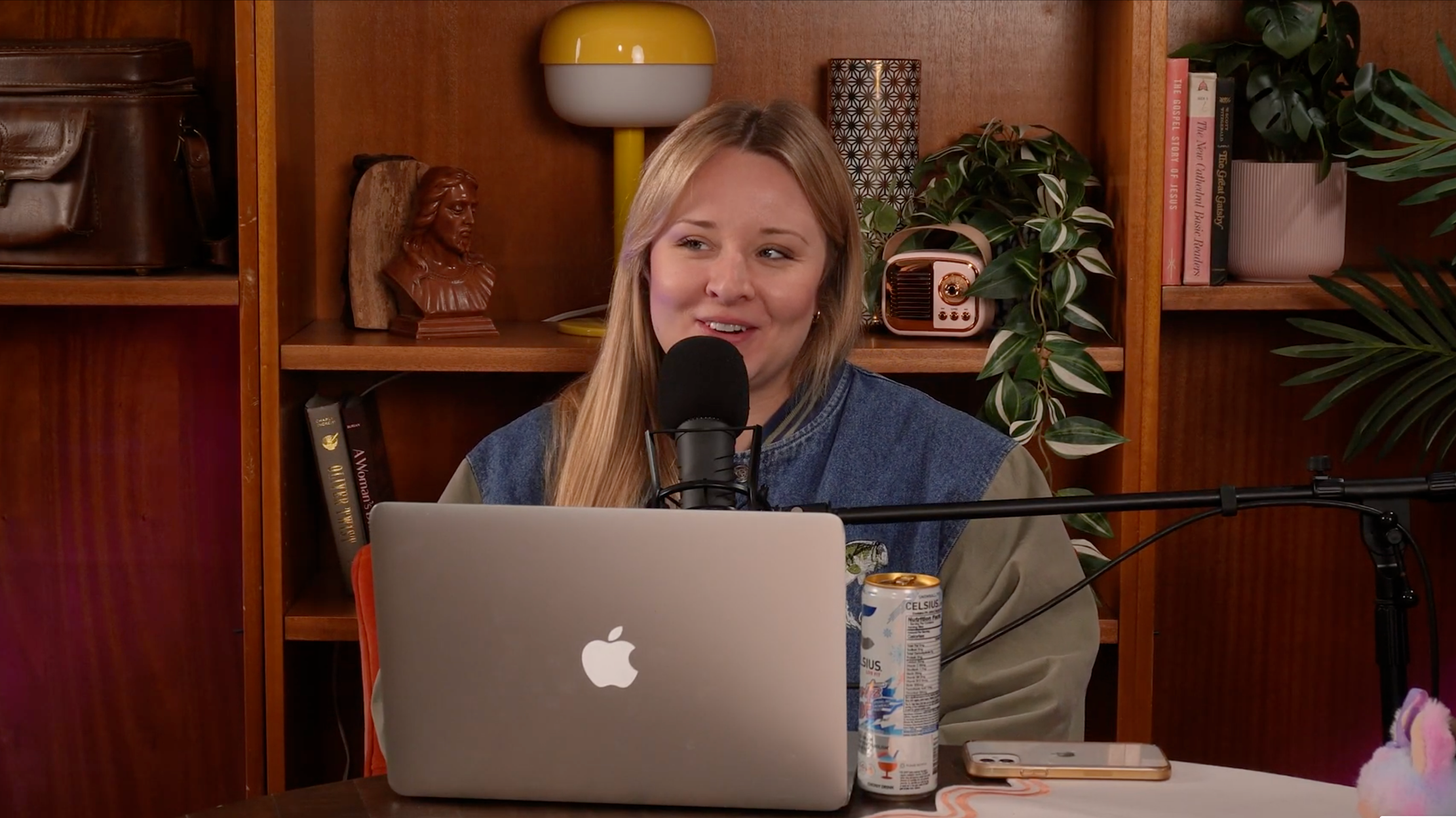 Bailee - podcast host has long blonde hair and is sitting in the studio in front of her laptop and microphone.