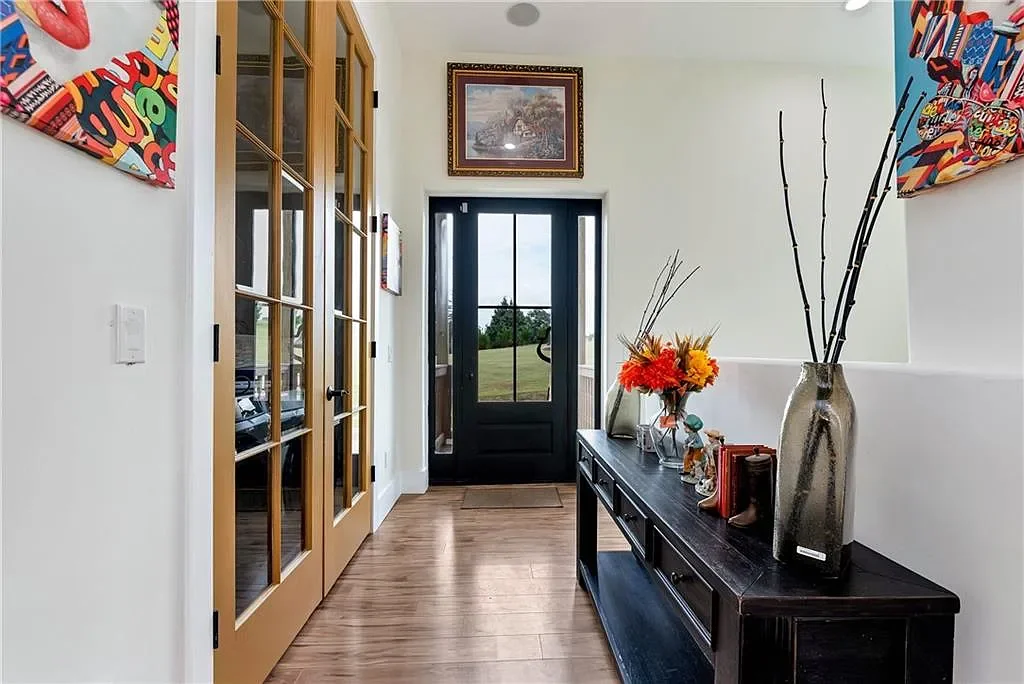 Entryway with a black front door, a wooden console table decorated with flowers and vases, and colorful abstract artwork on white walls.