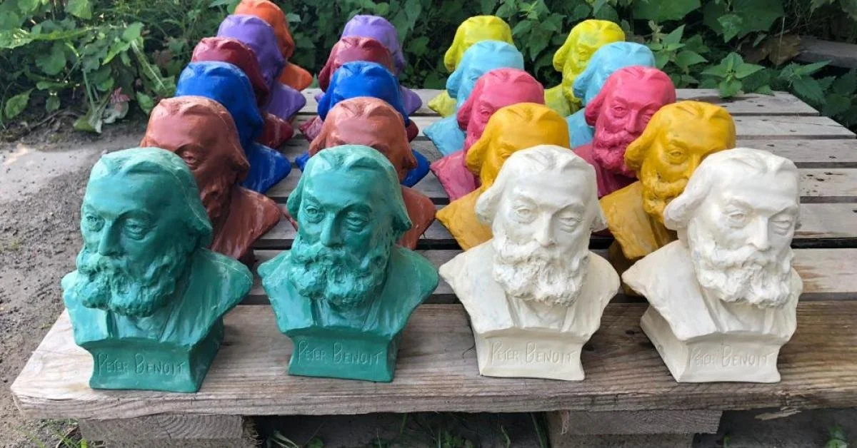 Colorful busts of the philosopher Peter Benoit lined up on a wooden surface outdoors.