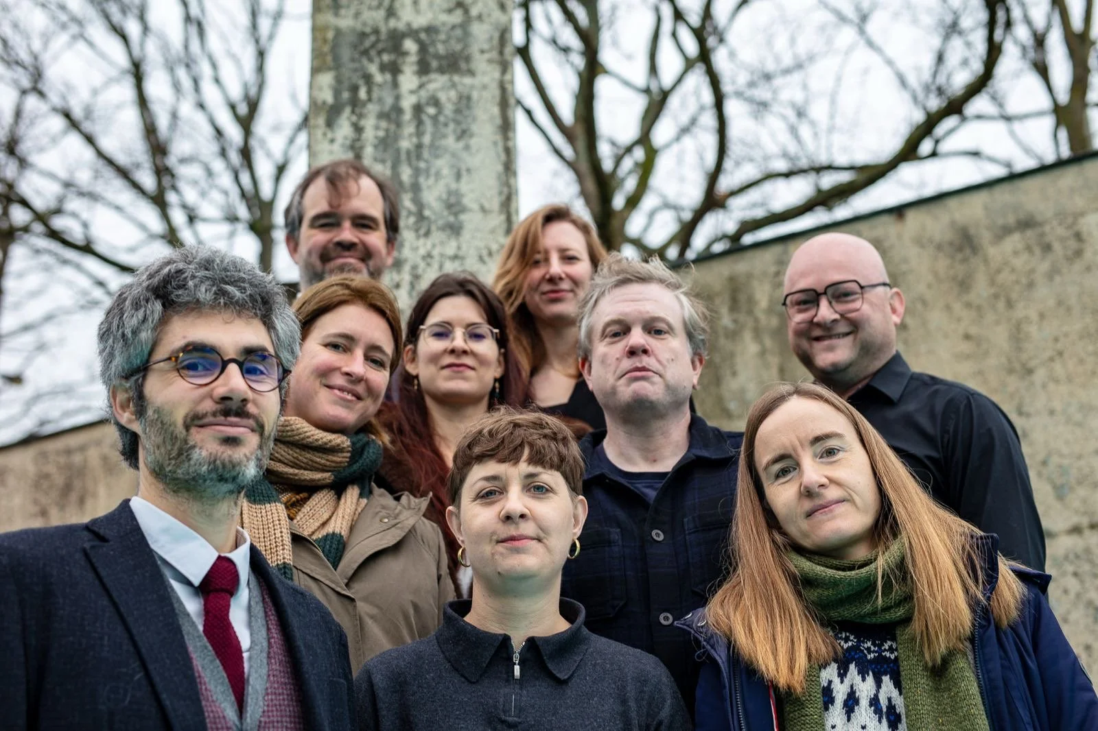 Group of ten adults outdoors, standing in front of trees and a stone wall, posing for a photo.