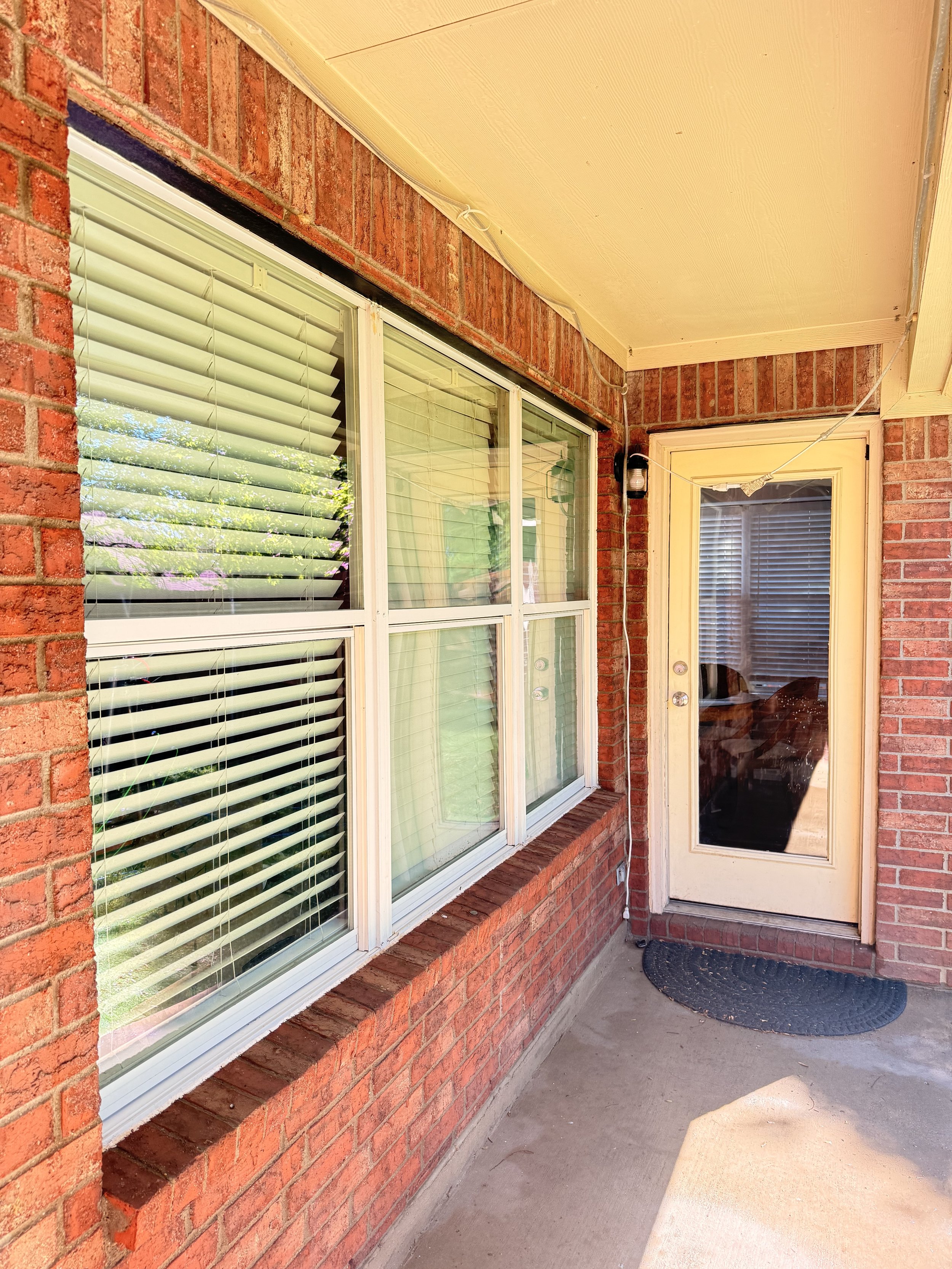 Brick house with three large windows featuring beige trim, window blinds, and a curved brick wall.