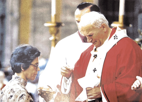 Une cérémonie religieuse avec un prêtre en robe rouge et une femme vêtue en habit traditionnel, dans un lieu religieux.