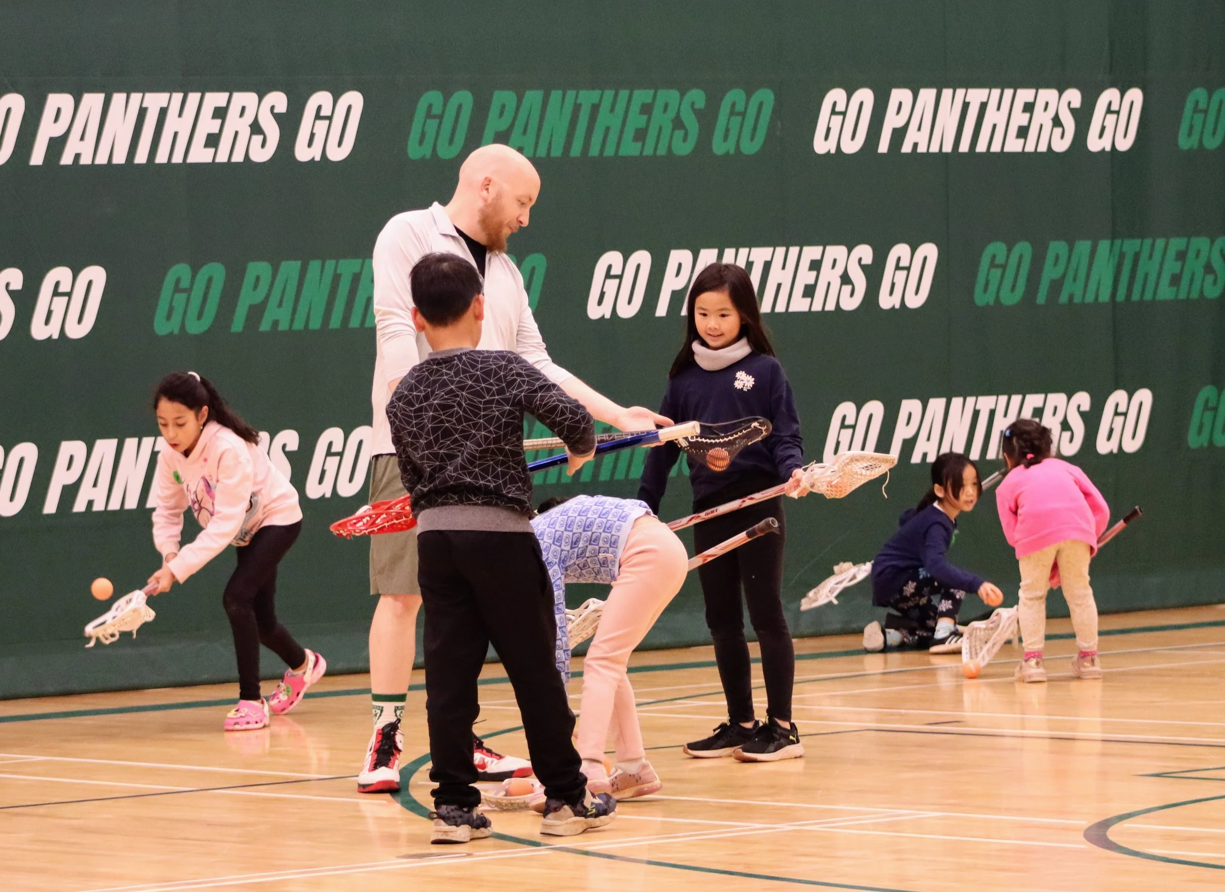 Indoor hockey practice with children and a coach, colorful hockey sticks, and a green wall with 'Go Panthers Go' text.