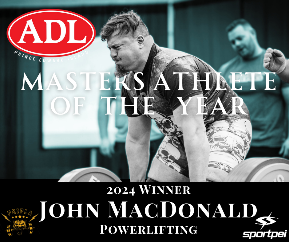 A man lifting weights during a powerlifting competition, wearing a T-shirt and skull-patterned shorts, with a focused expression. The background shows other people and a presentation screen. The image indicates John MacDonald as the 2024 Master Athle