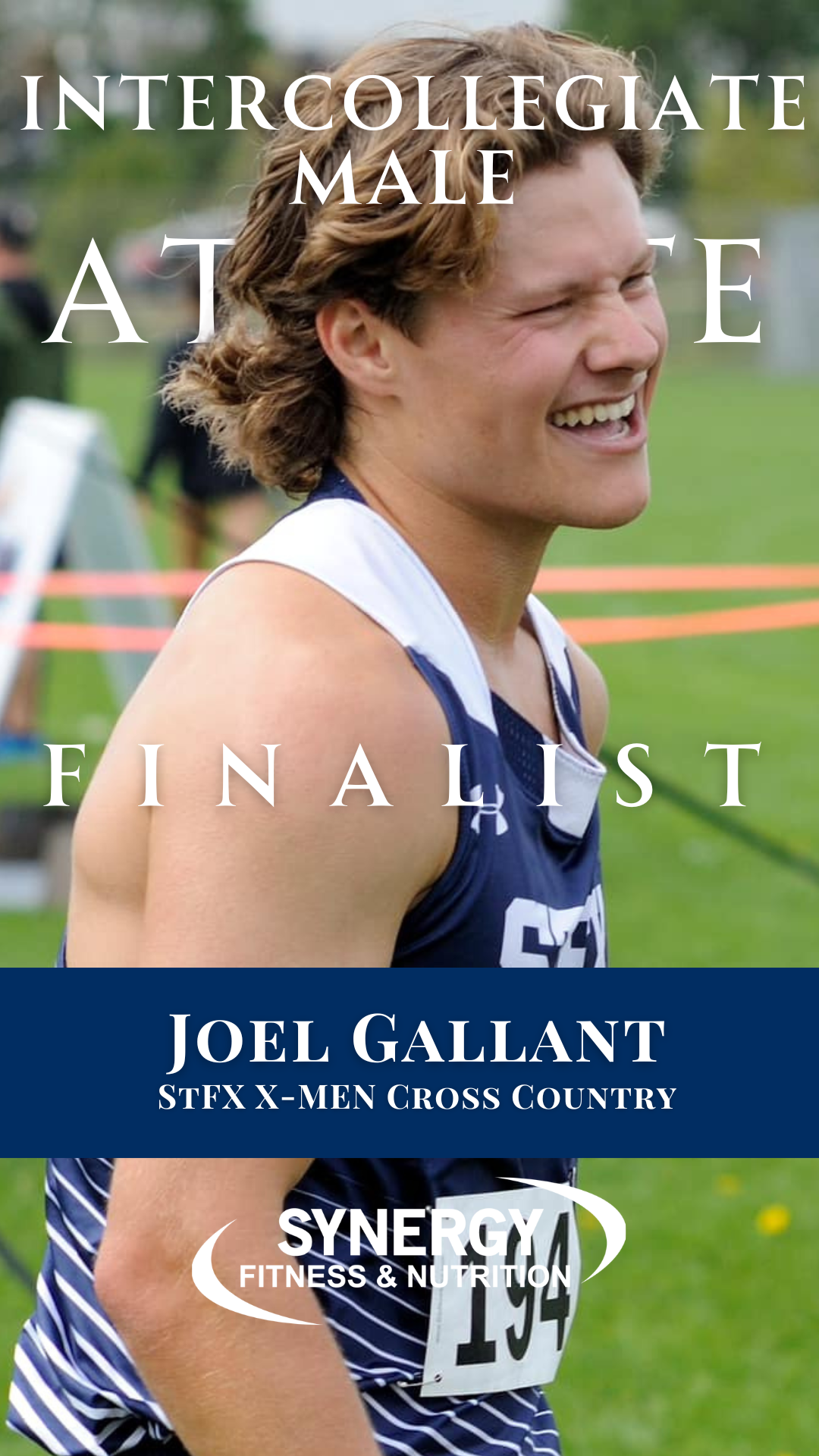 A young man smiling, wearing a blue athletic uniform with a number bib, outdoors on a grassy field with a blurred background of people, trees, and sports equipment.