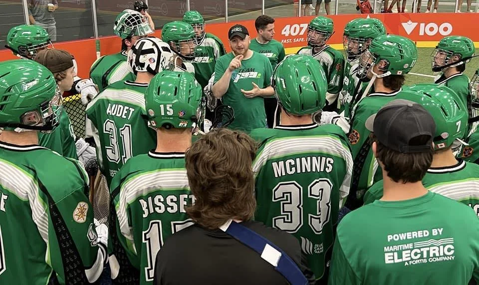 A group of ice hockey players in green jerseys and helmets gathered around a coach in an indoor rink, listening to instructions.