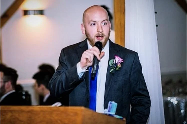 A man in a suit speaking into a microphone at a formal event.