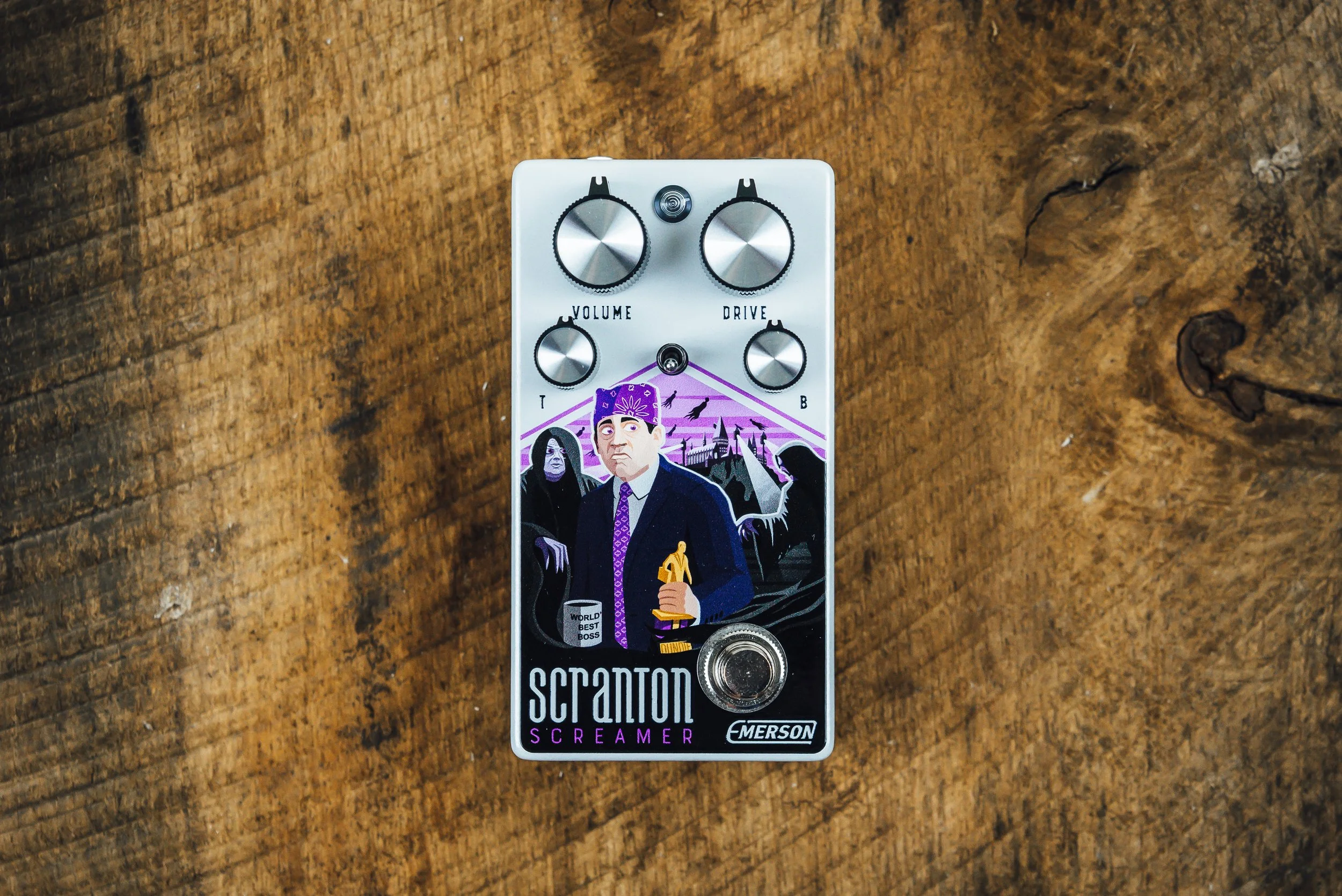 Guitar effects pedal with artwork featuring a man in a suit holding a golden award, surrounded by dark figures and a purple sky background.