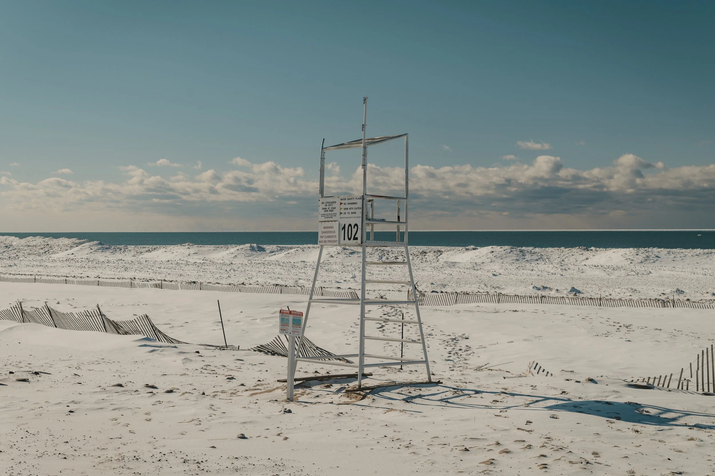 Empty lifeguard chair on a sandy beach with a cloudy sky and ocean in the background.