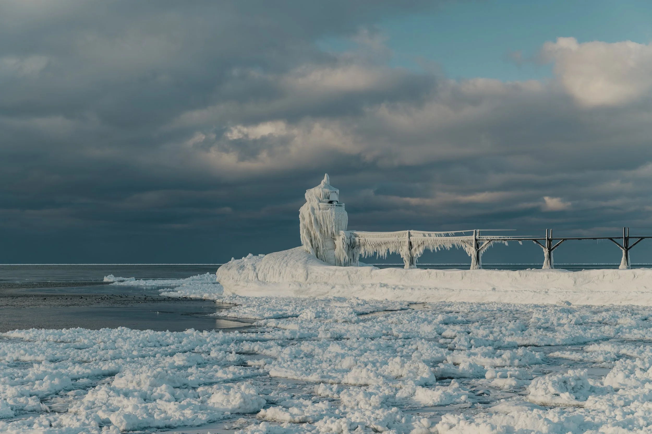 Frozen and ice-covered lighthouse on a snow-covered pier with a cloudy sky.