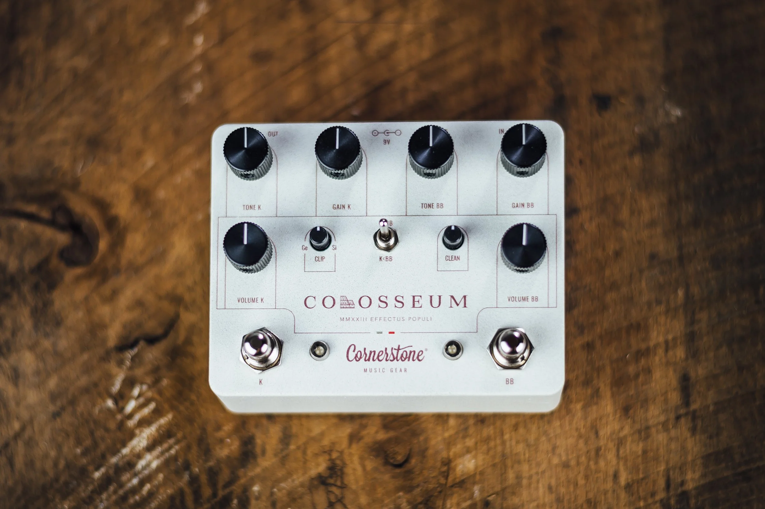 Overhead view of a white guitar effects pedal on a wooden surface with black knobs and labels.