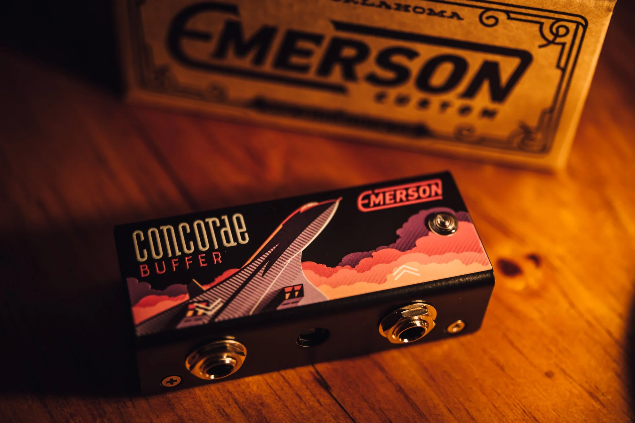 A guitar buffer pedal labeled 'Concorde Buffer' by Emerson with a colorful graphic design of clouds and a stylized aircraft on a wooden surface.