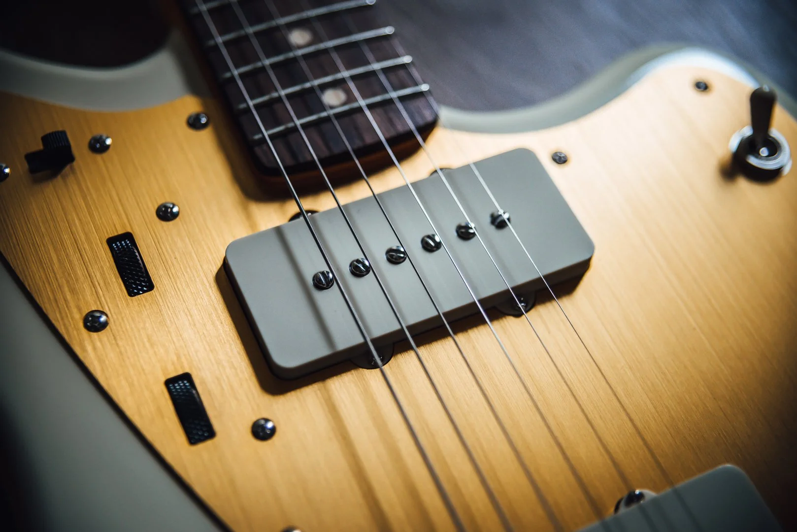 Close-up of an electric guitar with a natural wood finish, showing the bridge, pickups, and part of the fretboard. Squier JMascis