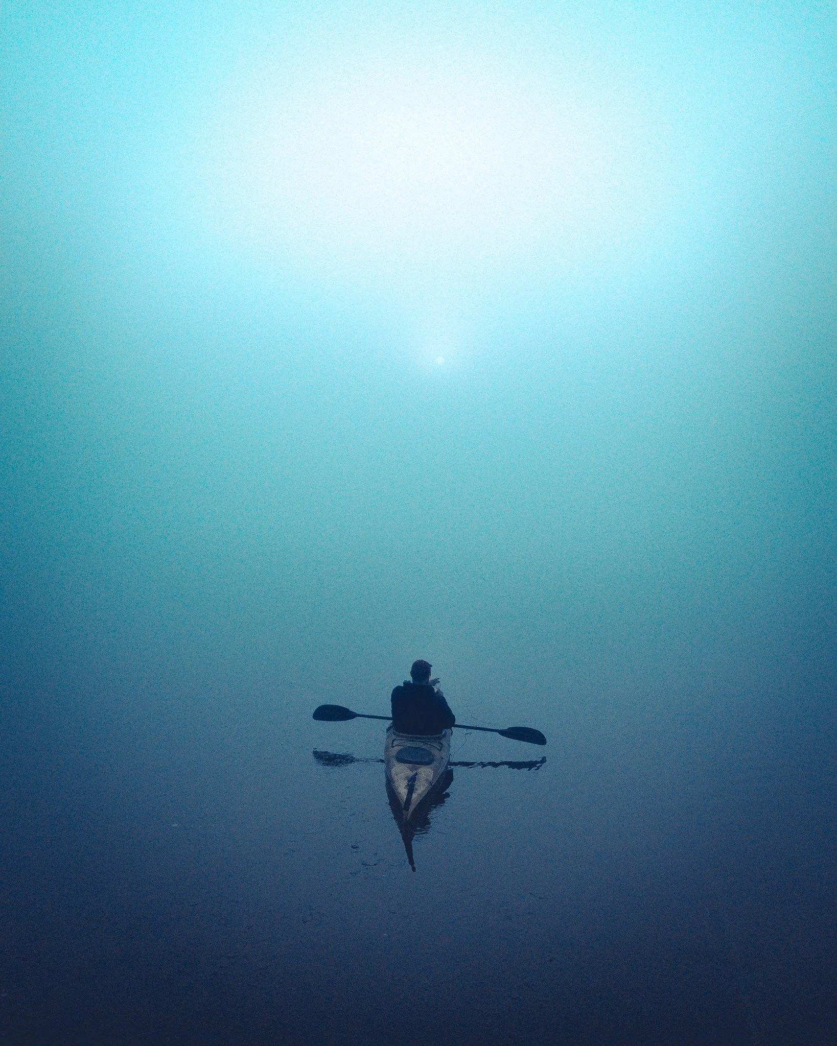 A person kayaking on calm water with a misty, blue-green gradient background.