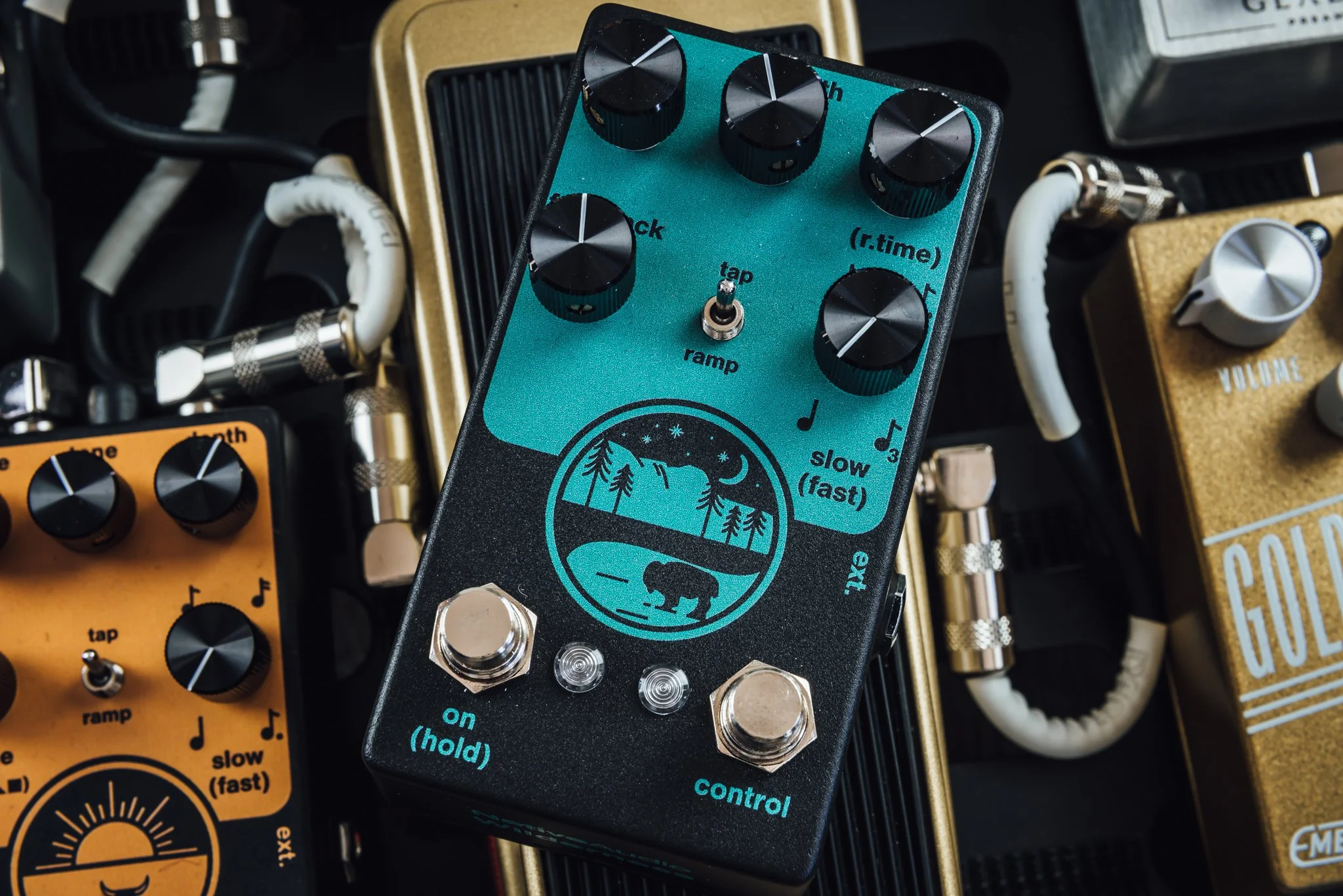 Electric guitar effects pedal with a nature scene illustration, multiple black control knobs, switches labeled on/off and control, surrounded by other guitar pedals and cables.