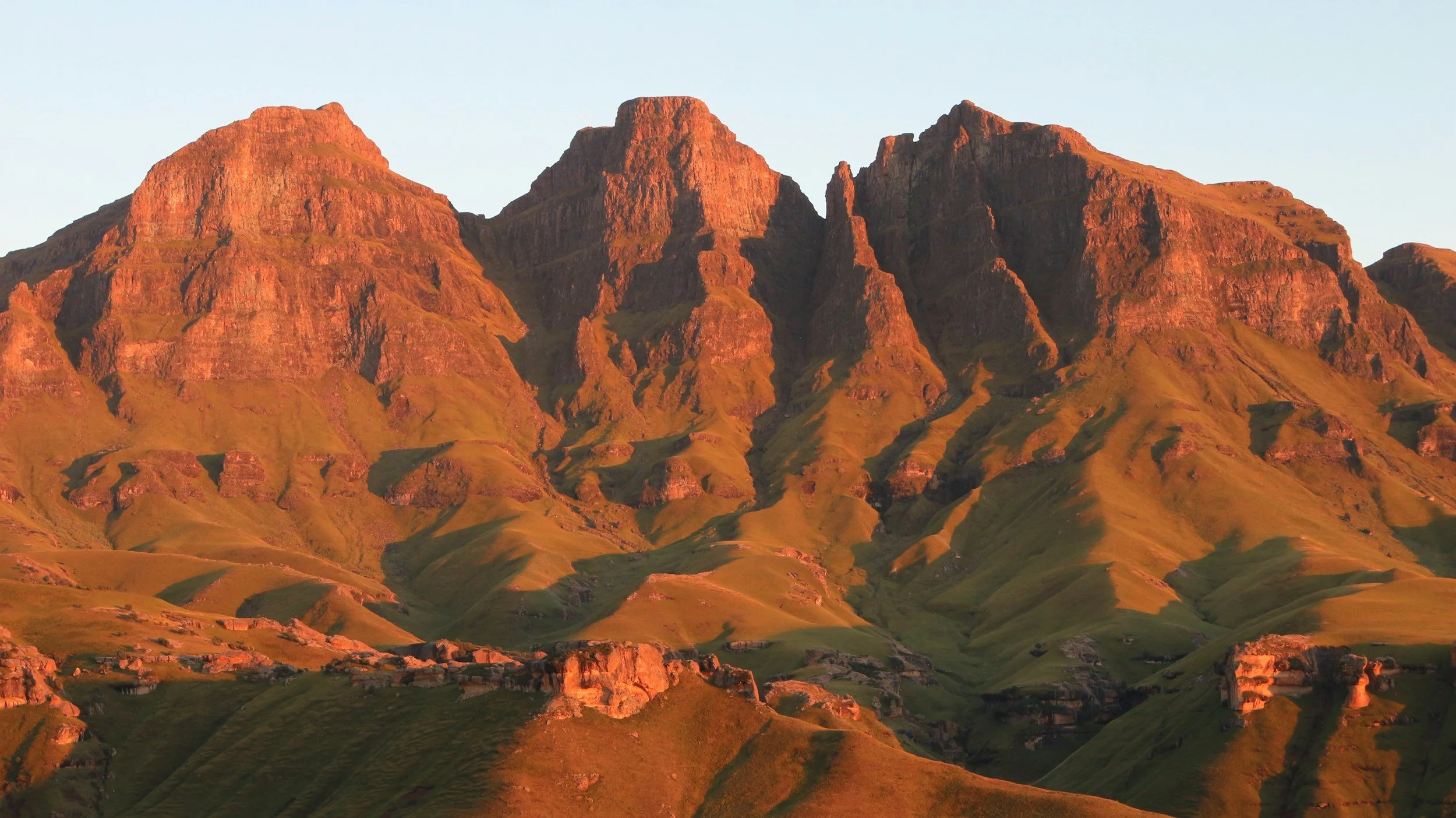 Sunset illuminating rugged mountain peaks and rolling green hills.