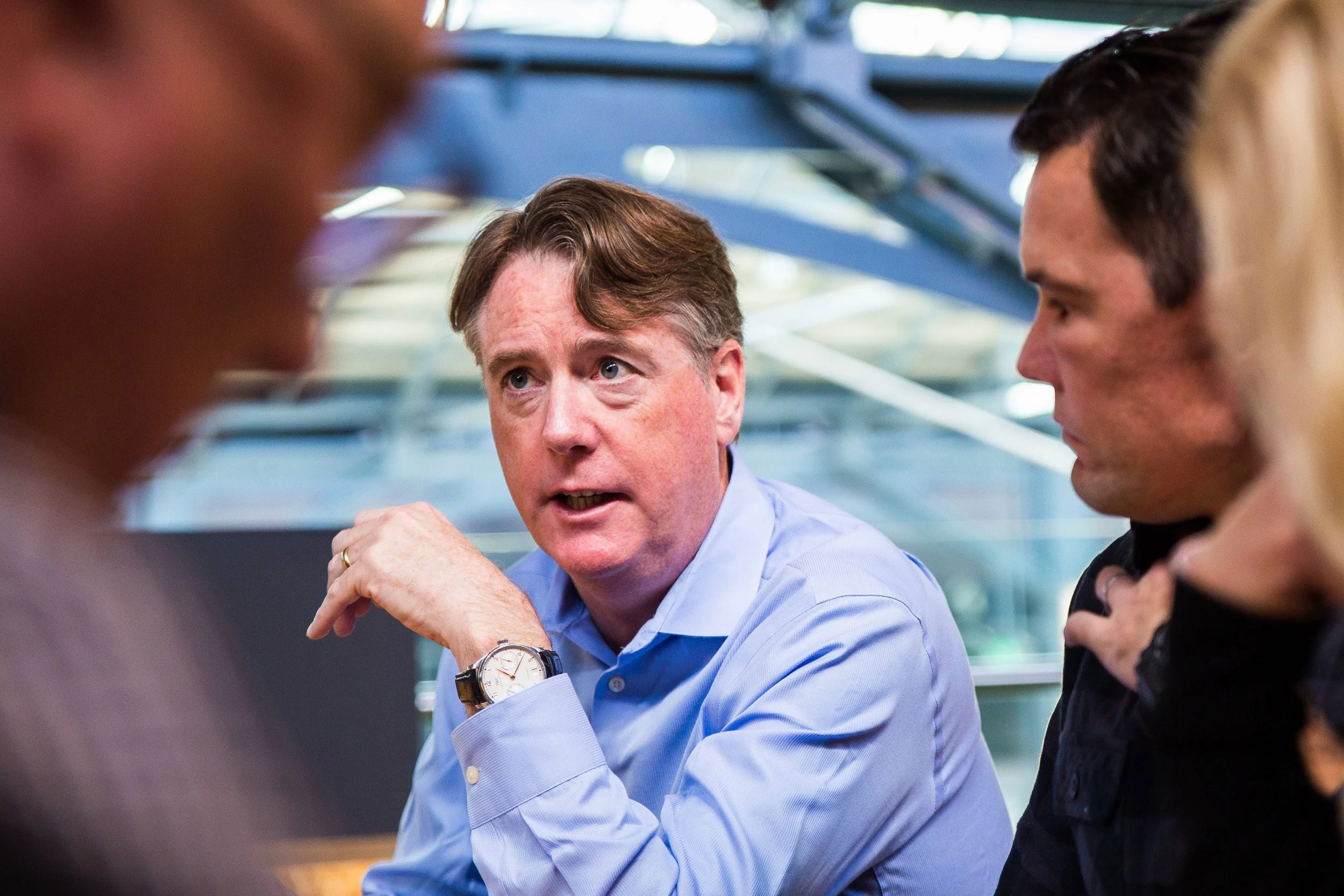 Aidan Connolly with a group of professionals engaged in discussion around a table in a modern industrial-style workspace, illustrating collaboration and leadership