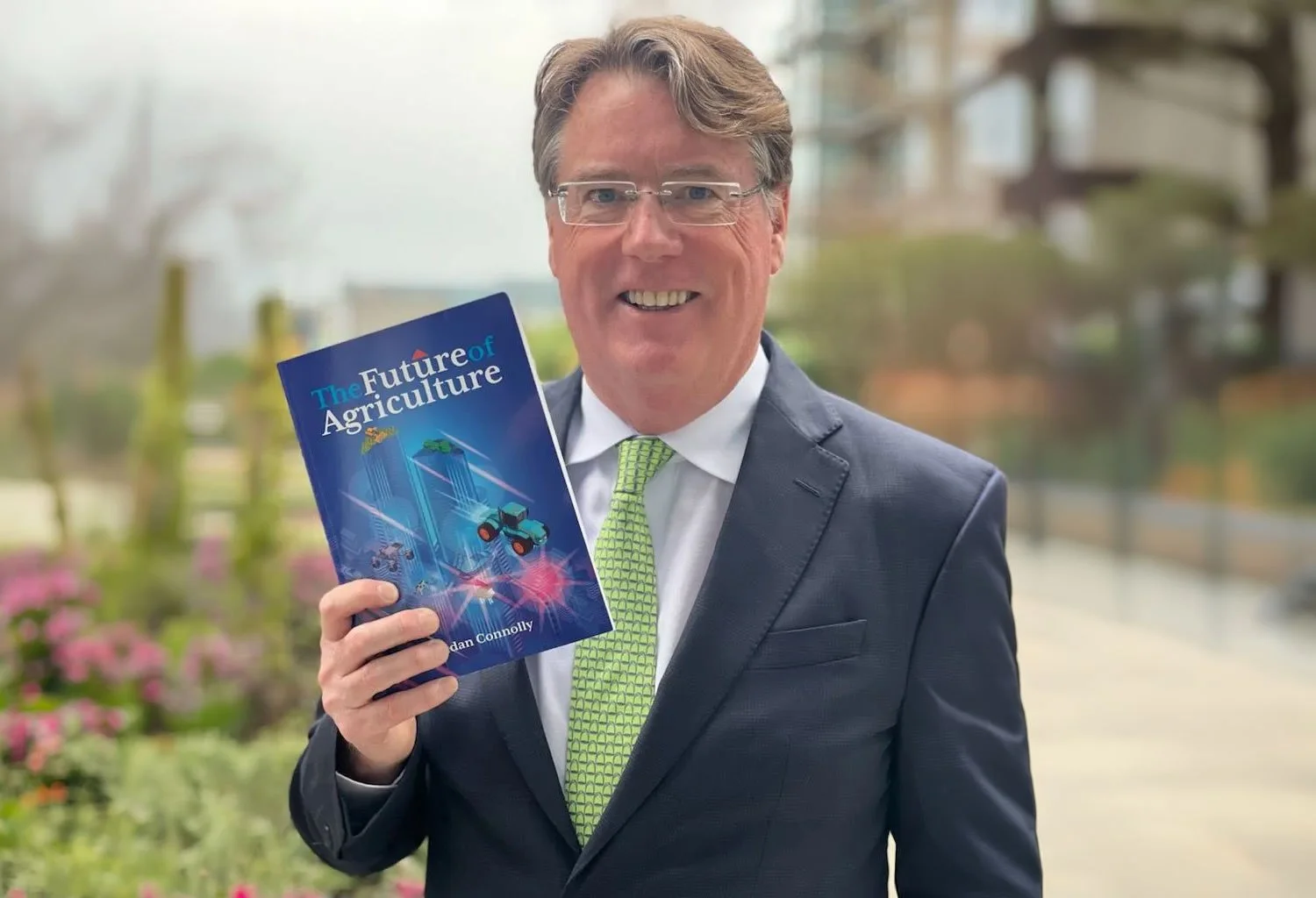 Business advisor holding ‘The Future of Agriculture’ book in an urban garden, symbolising innovation and leadership in modern agrifood systems.