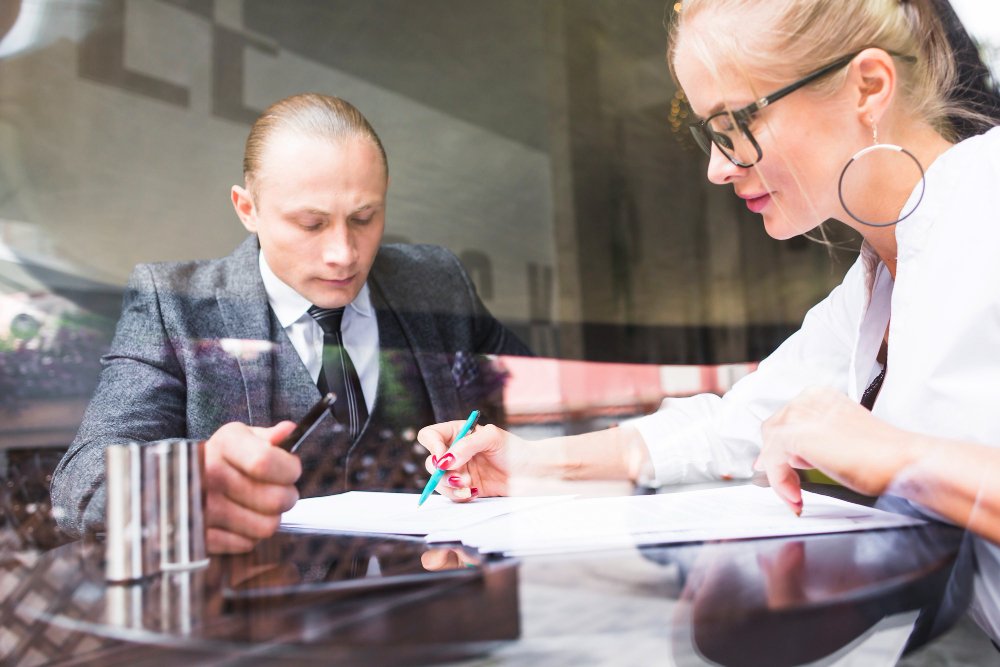 A man and a woman are seated at a meeting table, looking at documents on the table that represent how to lead and manage well