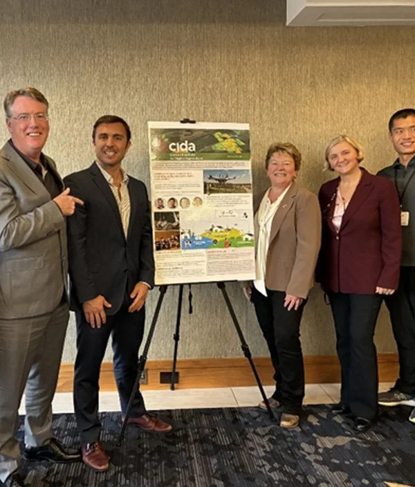 Five people standing next to a presentation poster on an easel in a conference room.
