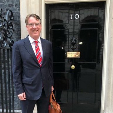 Professional advisor standing outside a formal government building entrance, symbolising strategic guidance for organisations navigating transformation and policy change.