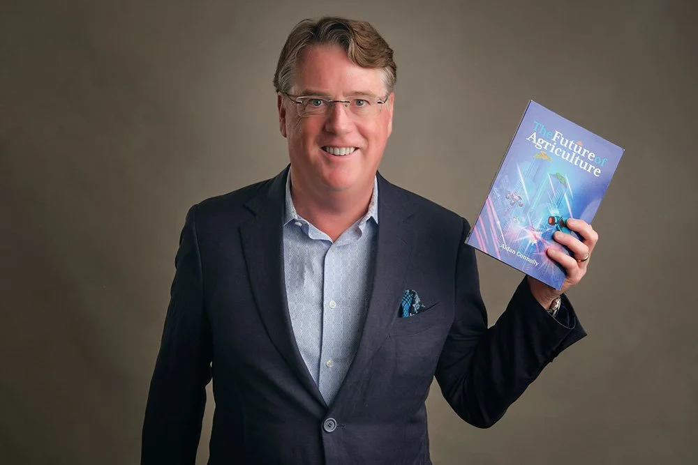 A man in a suit holding a book titled "The Future of Agriculture" and smiling at the camera.