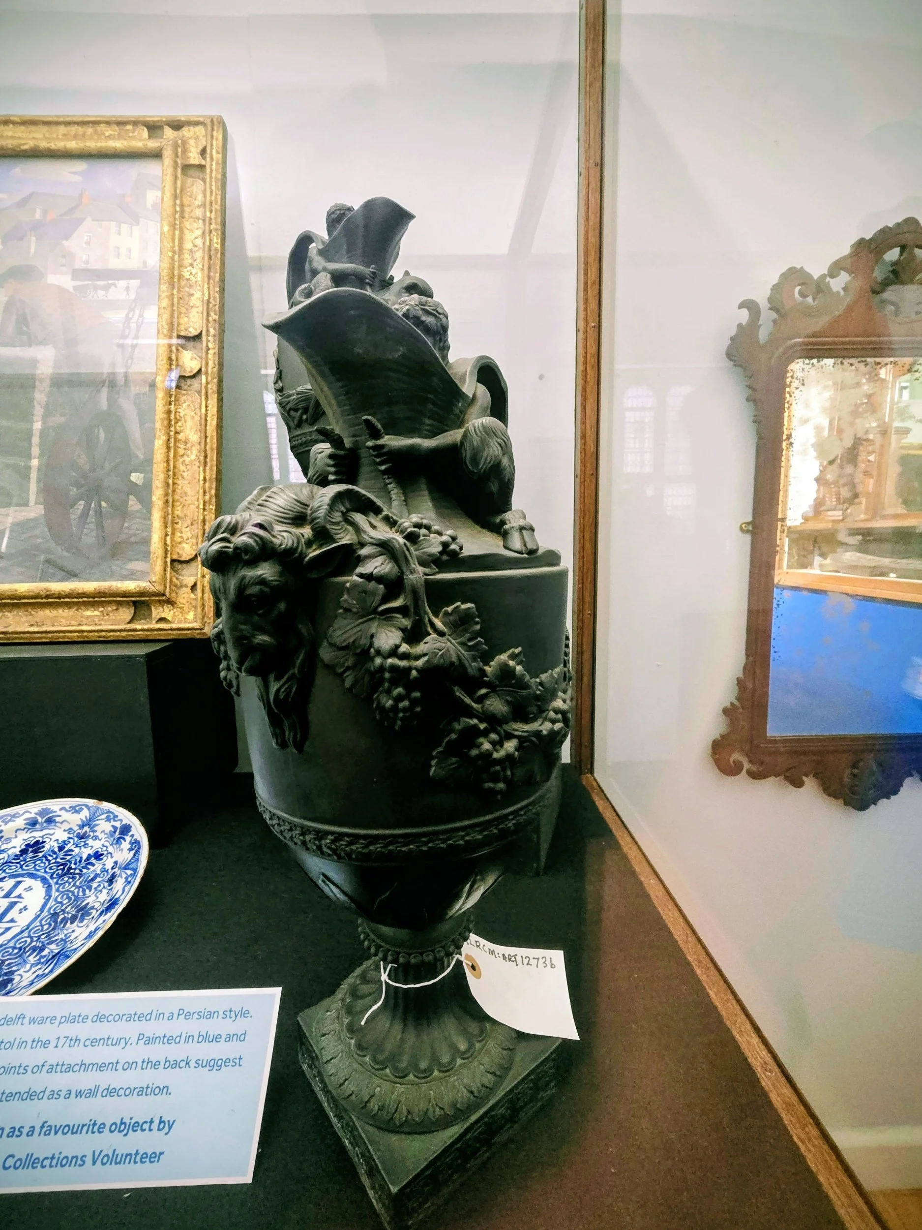 A black decorative vessel with a lion and grapevine motif, displayed in a glass case at a museum.