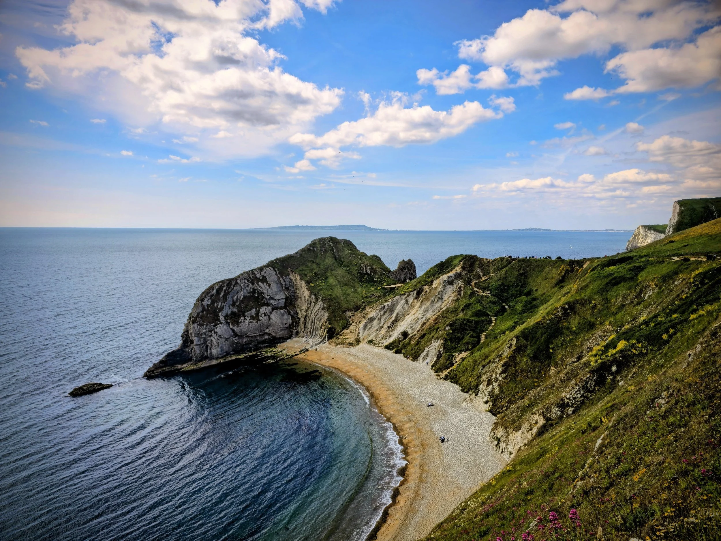 Coastal landscape along the Jurassic Coast showing steep cliffs, pebble beach, and expansive sea under an open sky.
