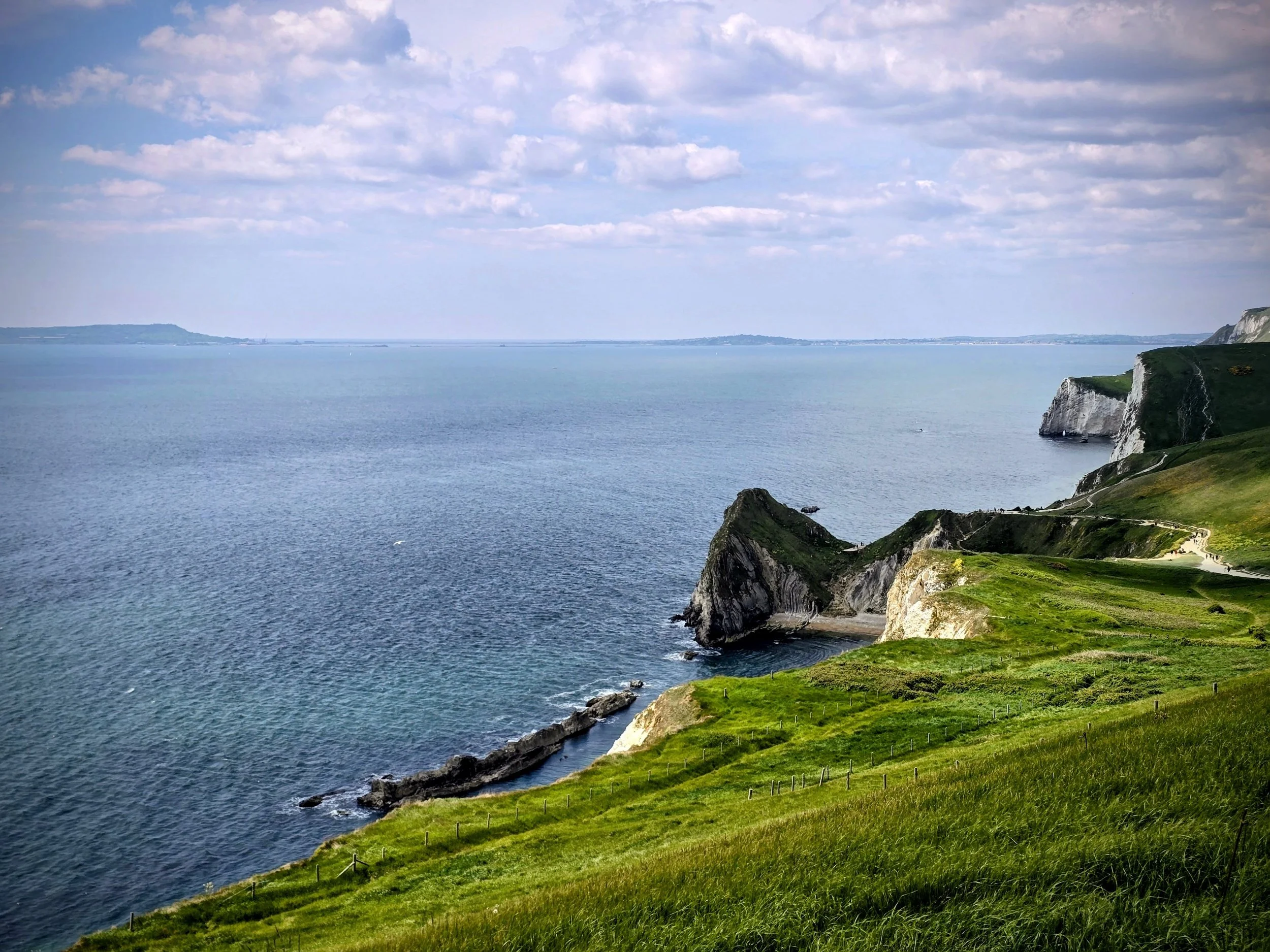 Coastal landscape along the Jurassic Coast showing steep cliffs, pebble beach, and expansive sea under an open sky.
