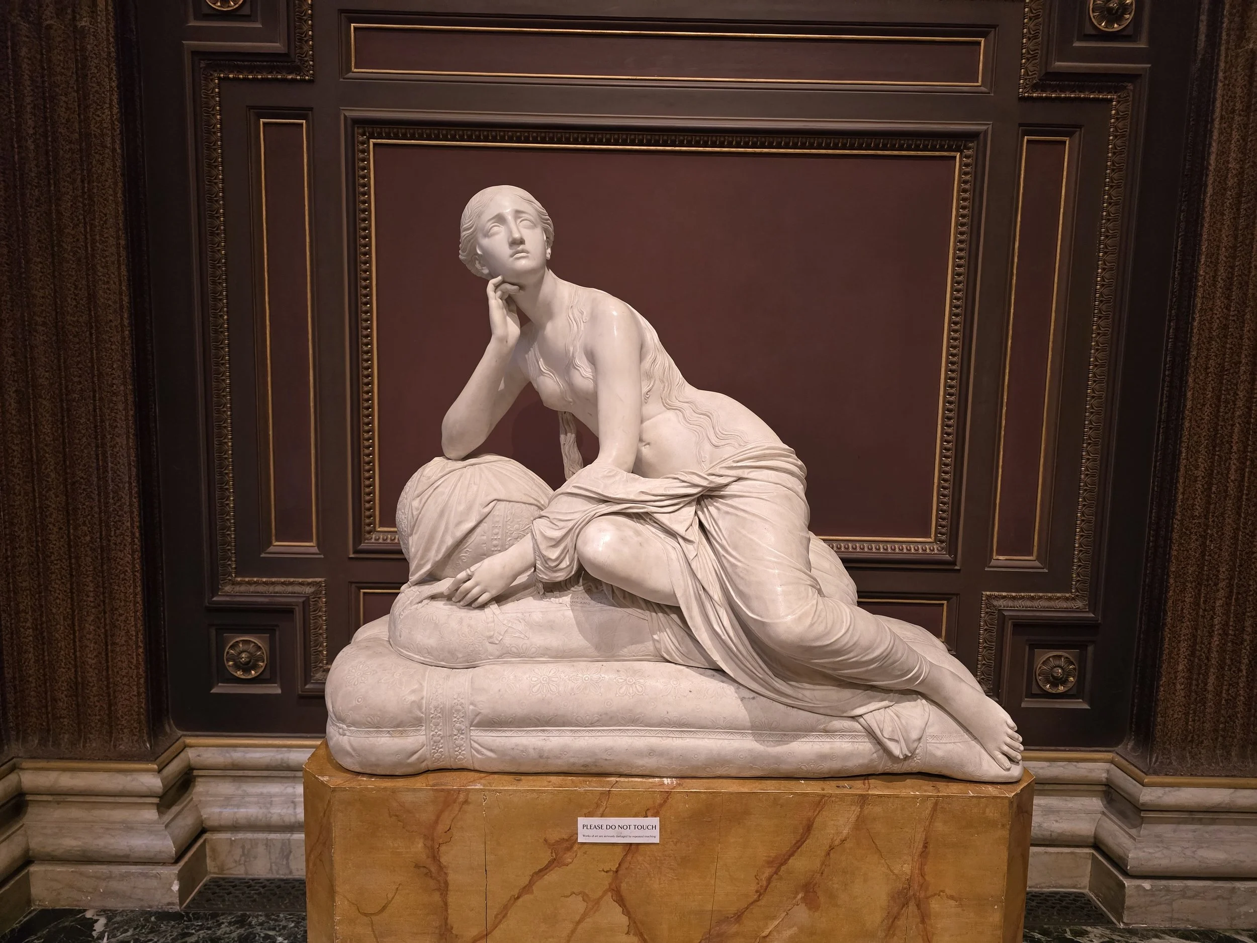 La Pia Contrita or Maddalena: M.7-1974
Figure of a partly draped nude woman with long hair dressed in Grecian style, seated on two rounded rectangular cushions, with her left leg extended behind her and her right bent up underneath her, She leans for