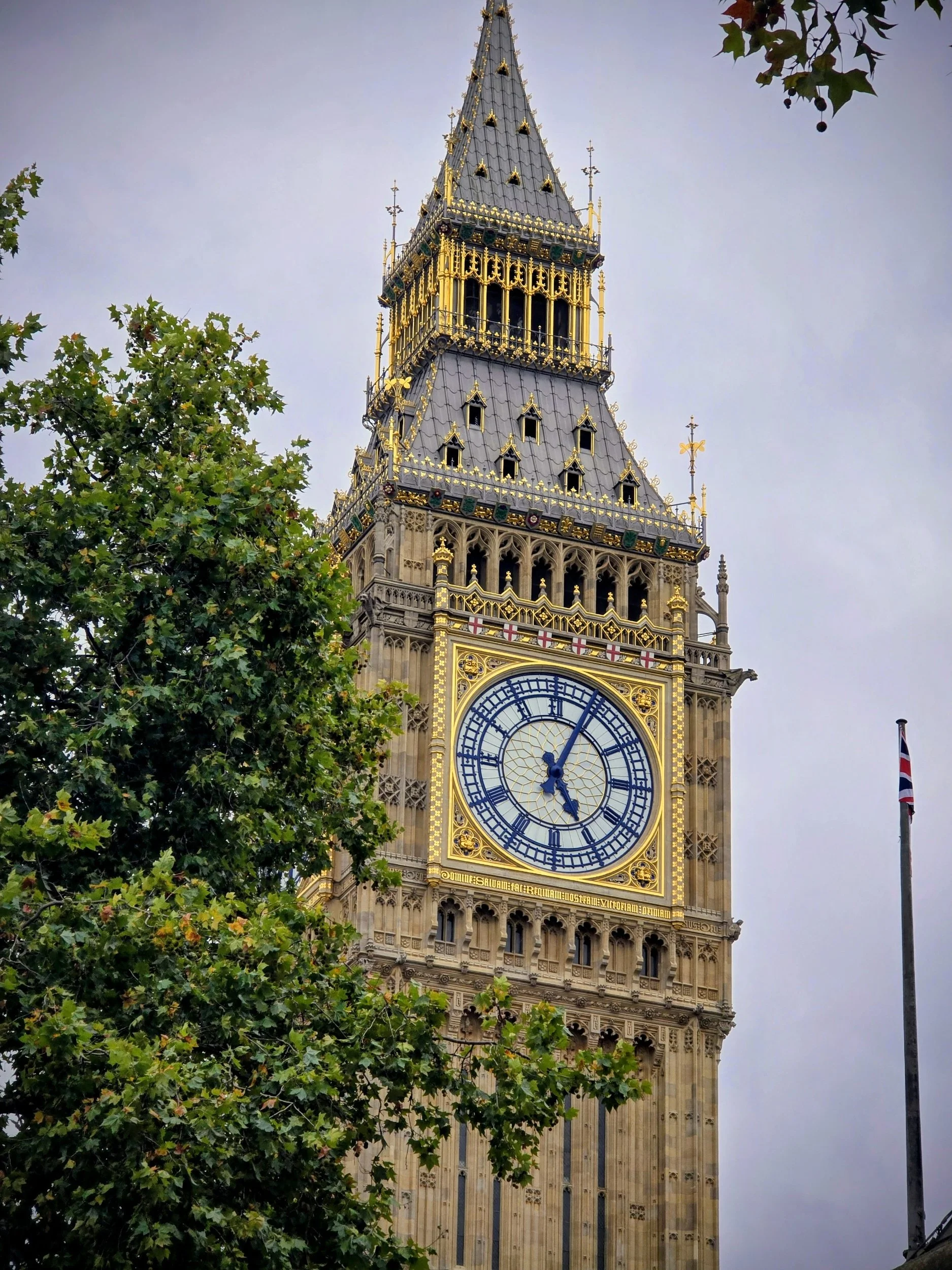 Big Ben clock tower in London with cloudy sky and surrounding trees.