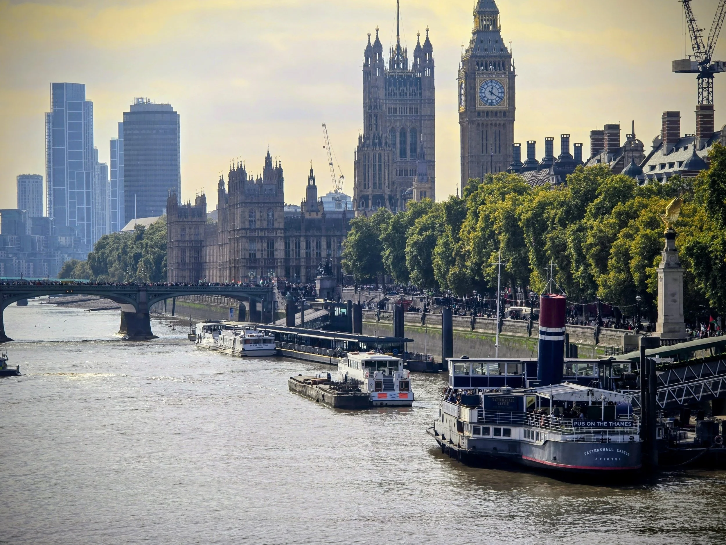 London skyline with Big Ben, the Houses of Parliament, and Thames River with boats docked along the riverbank.