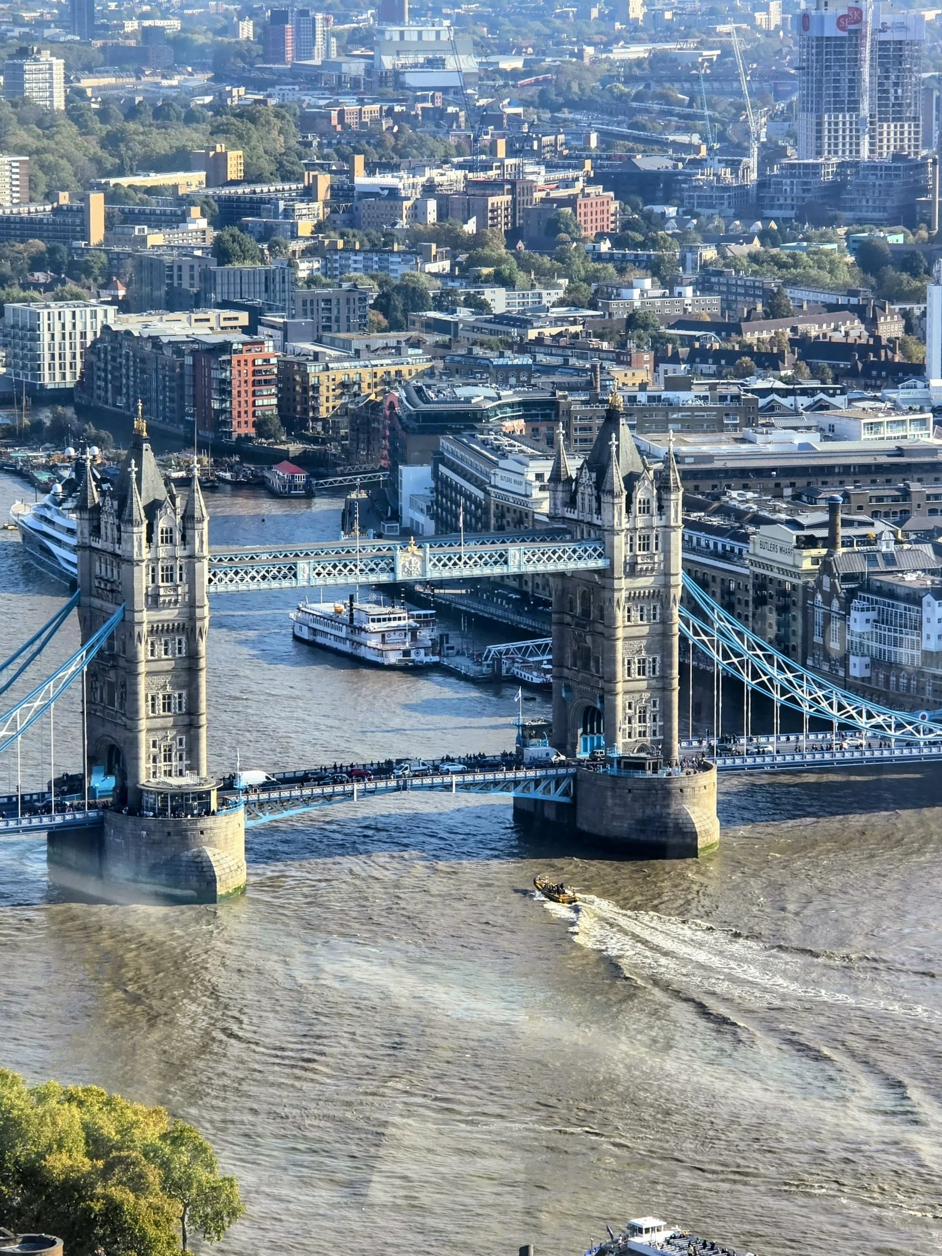 Aerial view of Tower Bridge crossing the River Thames in London, with boats and city buildings in the background.
