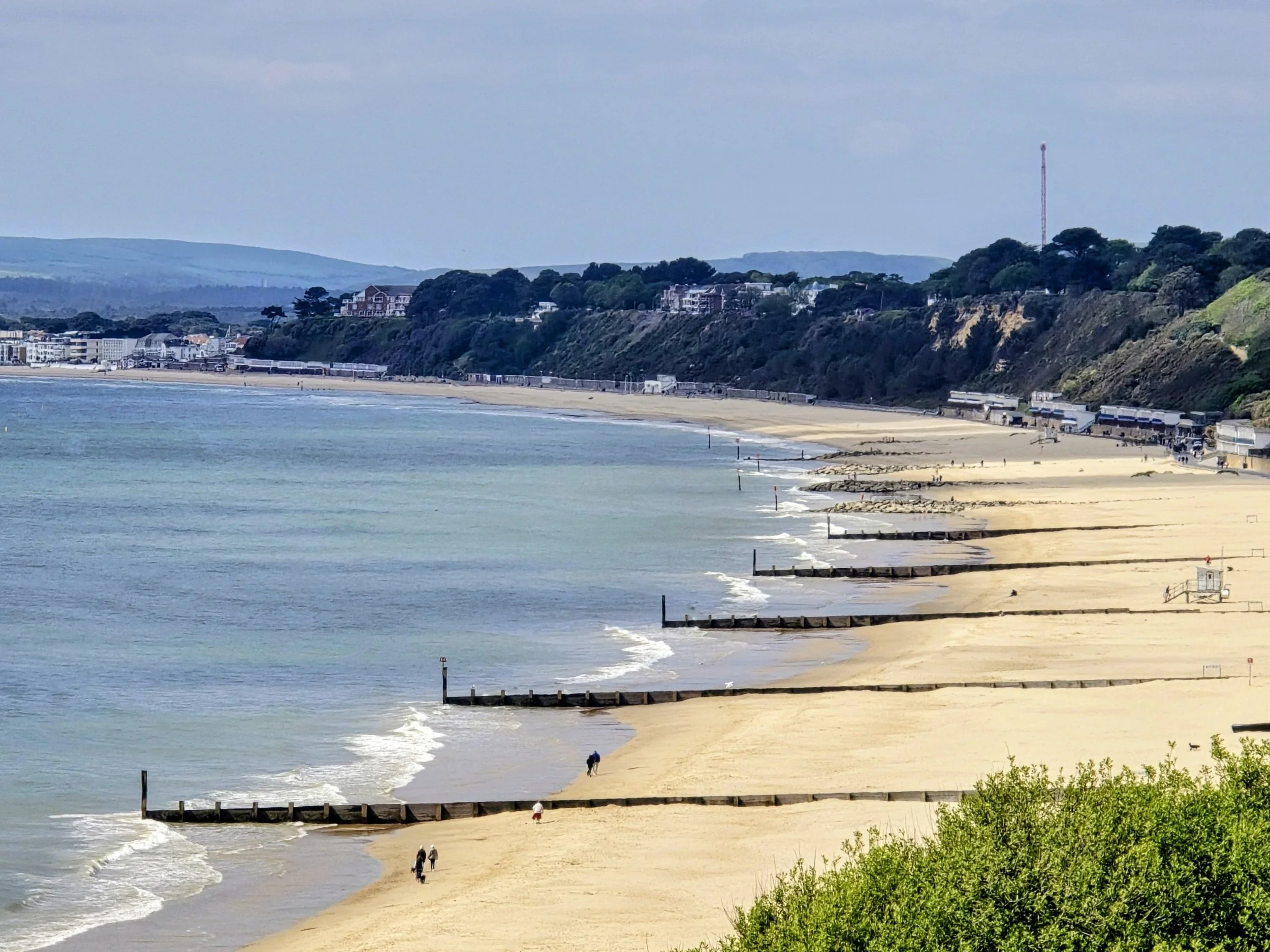 Scenic view of Bournemouth Beach with golden sand, gentle waves along the shoreline, and a wide coastal horizon under a bright sky.