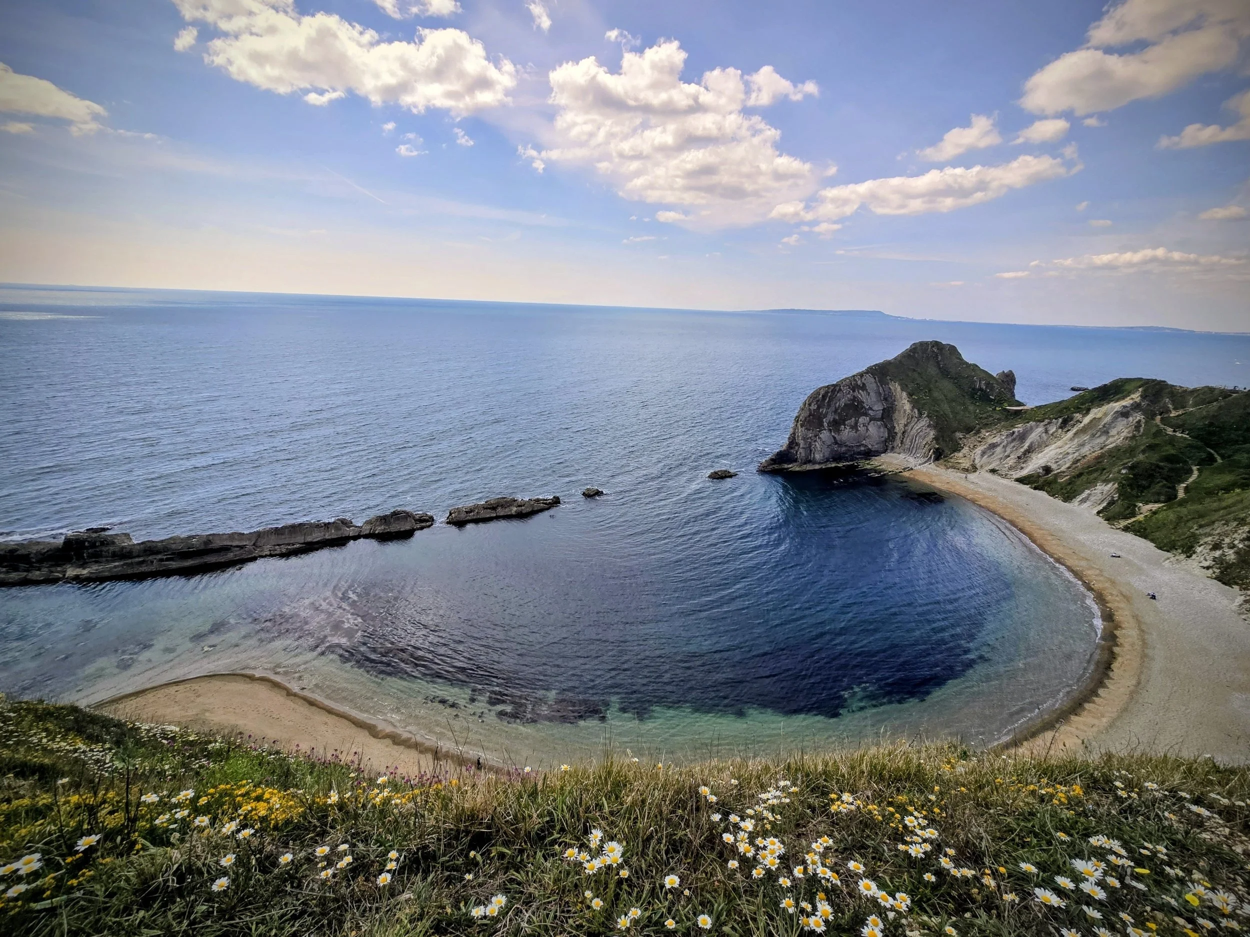 Panoramic photo of the Jurassic Coast featuring layered cliffs, blue ocean waters, and a rugged natural coastline.