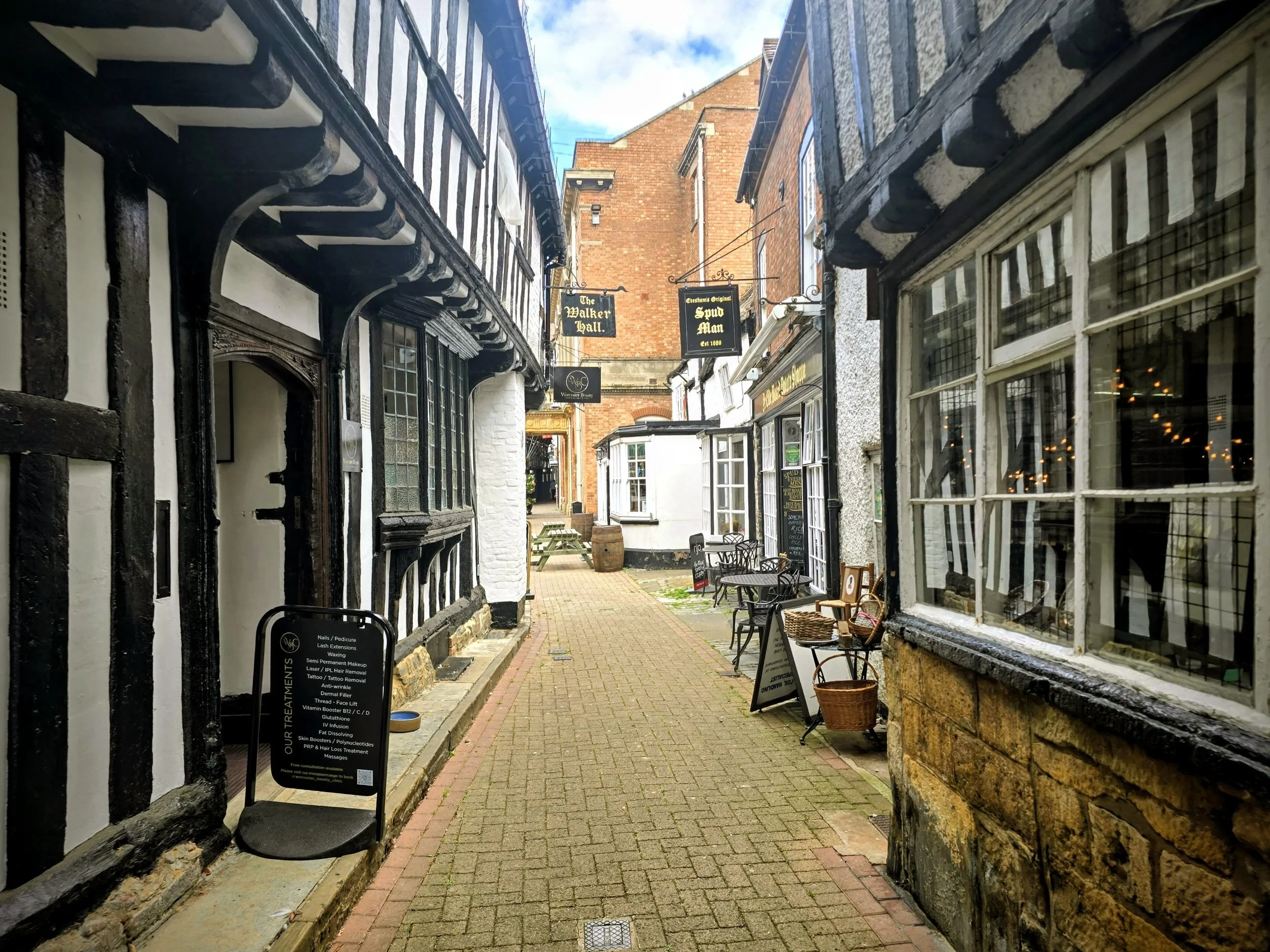 Historic Evesham high street featuring traditional half-timbered buildings, stone architecture, and local shops under a clear blue Cotswold sky.