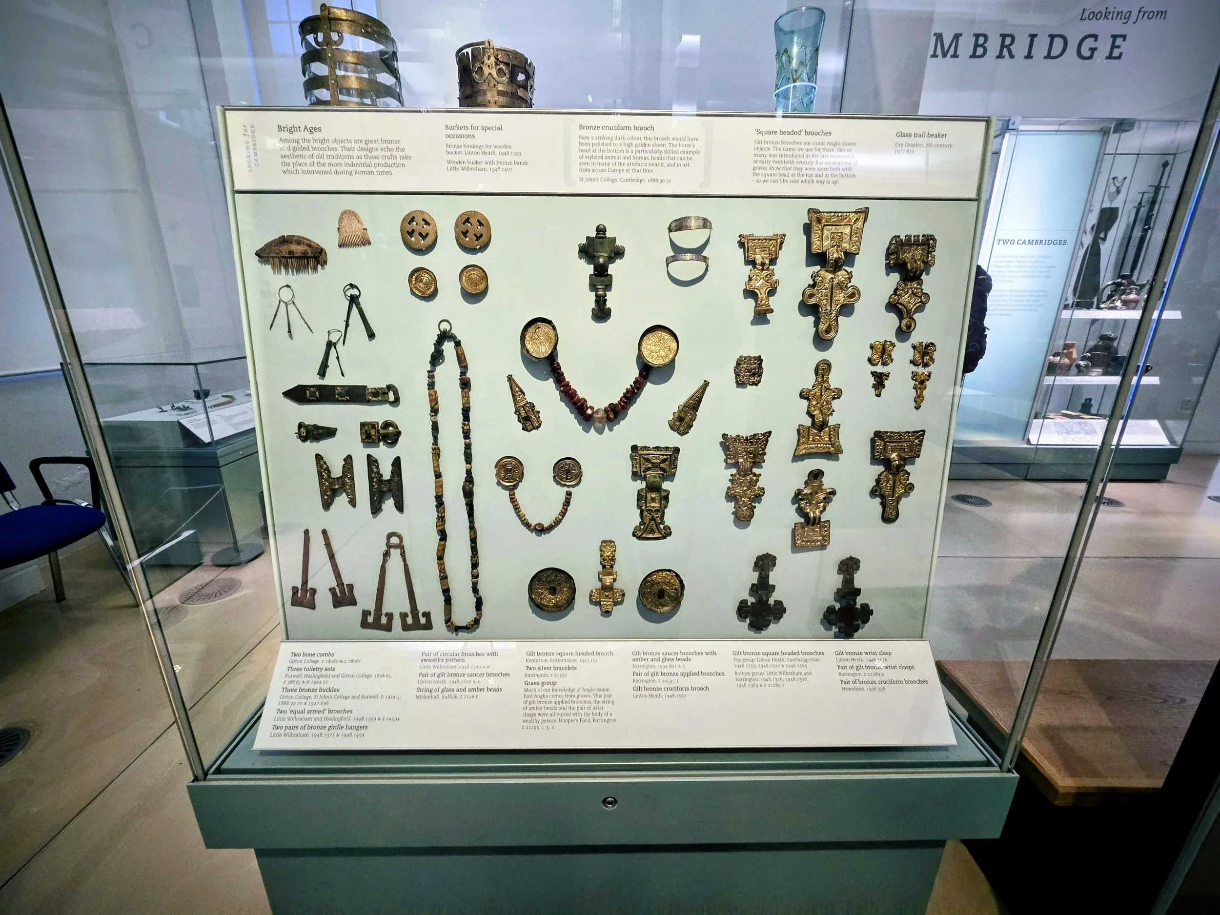 Display case with ancient jewelry and metal artifacts, including brooches, arm guards, buckles, and beads, from the Bright Ages and other periods.