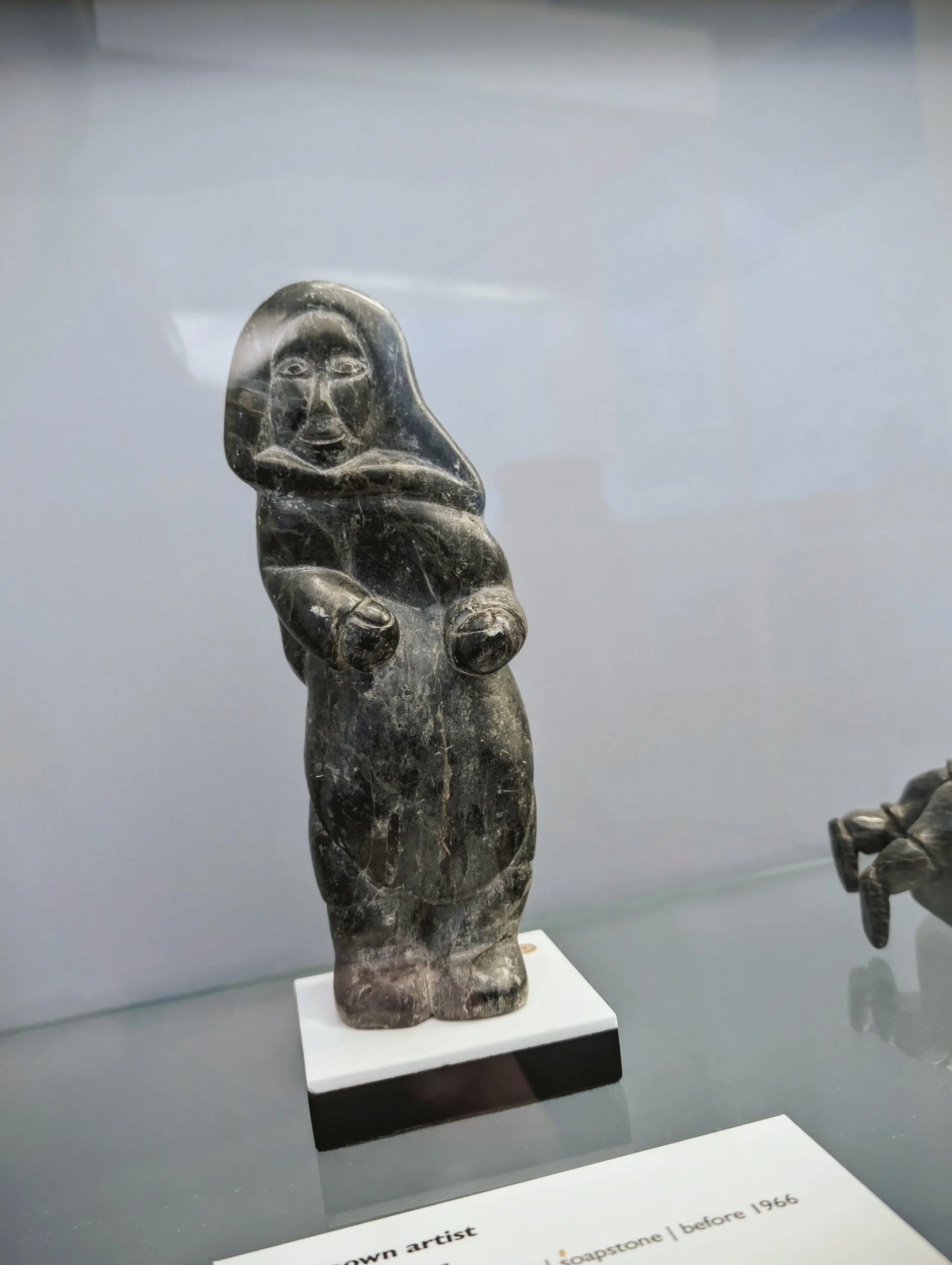 Stone sculpture of a humanoid figure with exaggerated features, displayed in a museum case.