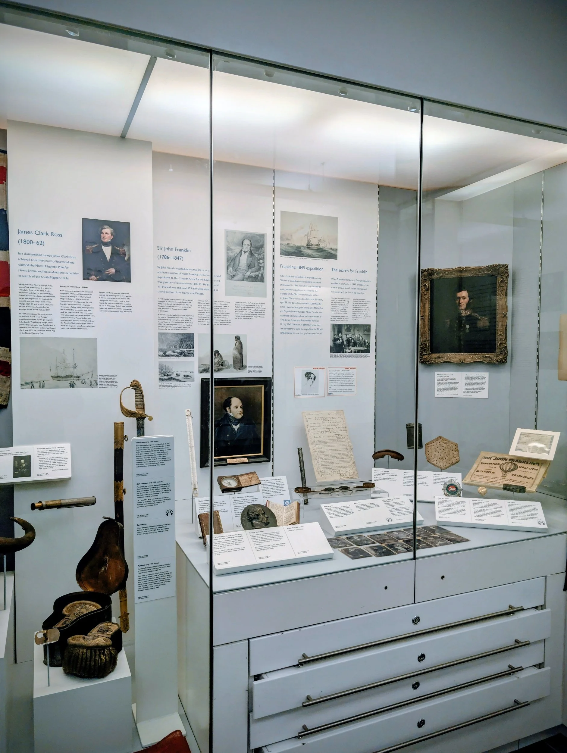 Museum display case with historical documents, photographs, and artifacts related to Sir John Franklin's Arctic expeditions, including portraits and written materials.