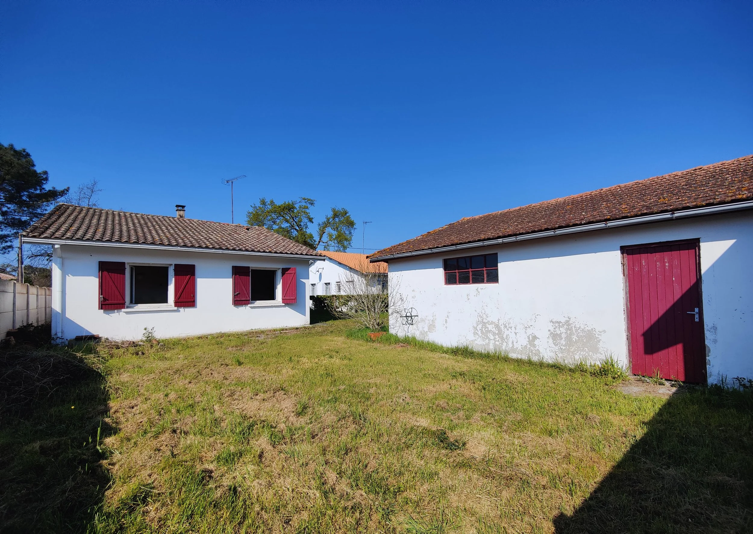 Cabanes en pierre avec murs blancs et volets rouges dans un jardin ensoleillé, sous un ciel bleu clair à cazaux