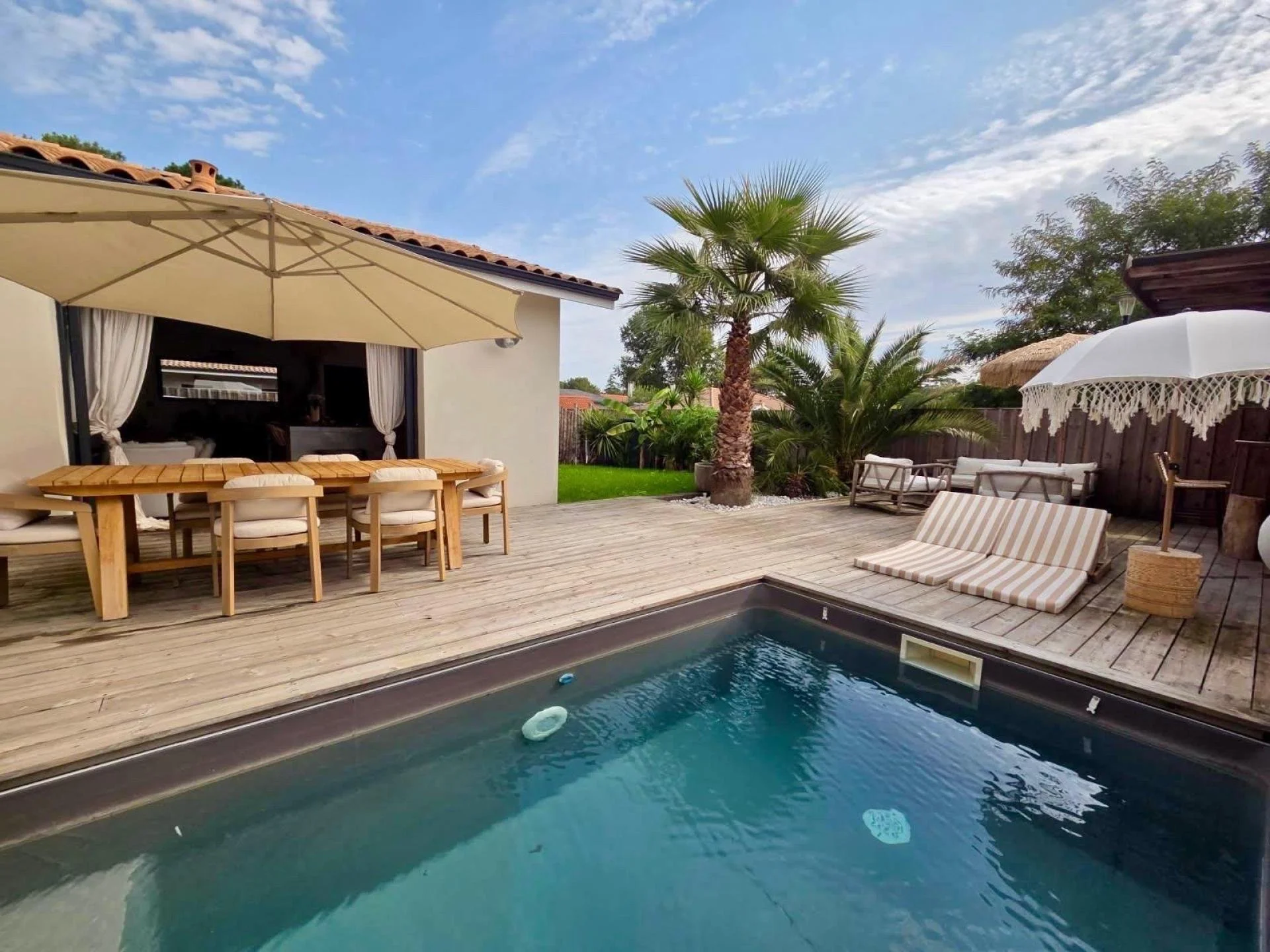 Terrasse avec piscine, meubles de détente, parasols et palmier dans un jardin.