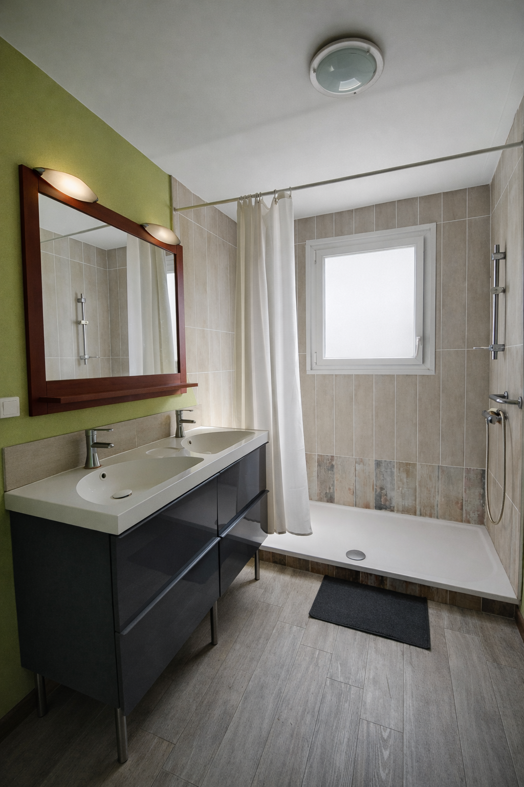 Salle de bain avec double lavabo, miroir avec éclairage, douche avec paroi en tissu blanc, fenêtre, carrelage beige, sol en bois gris, tapis noir à cazaux