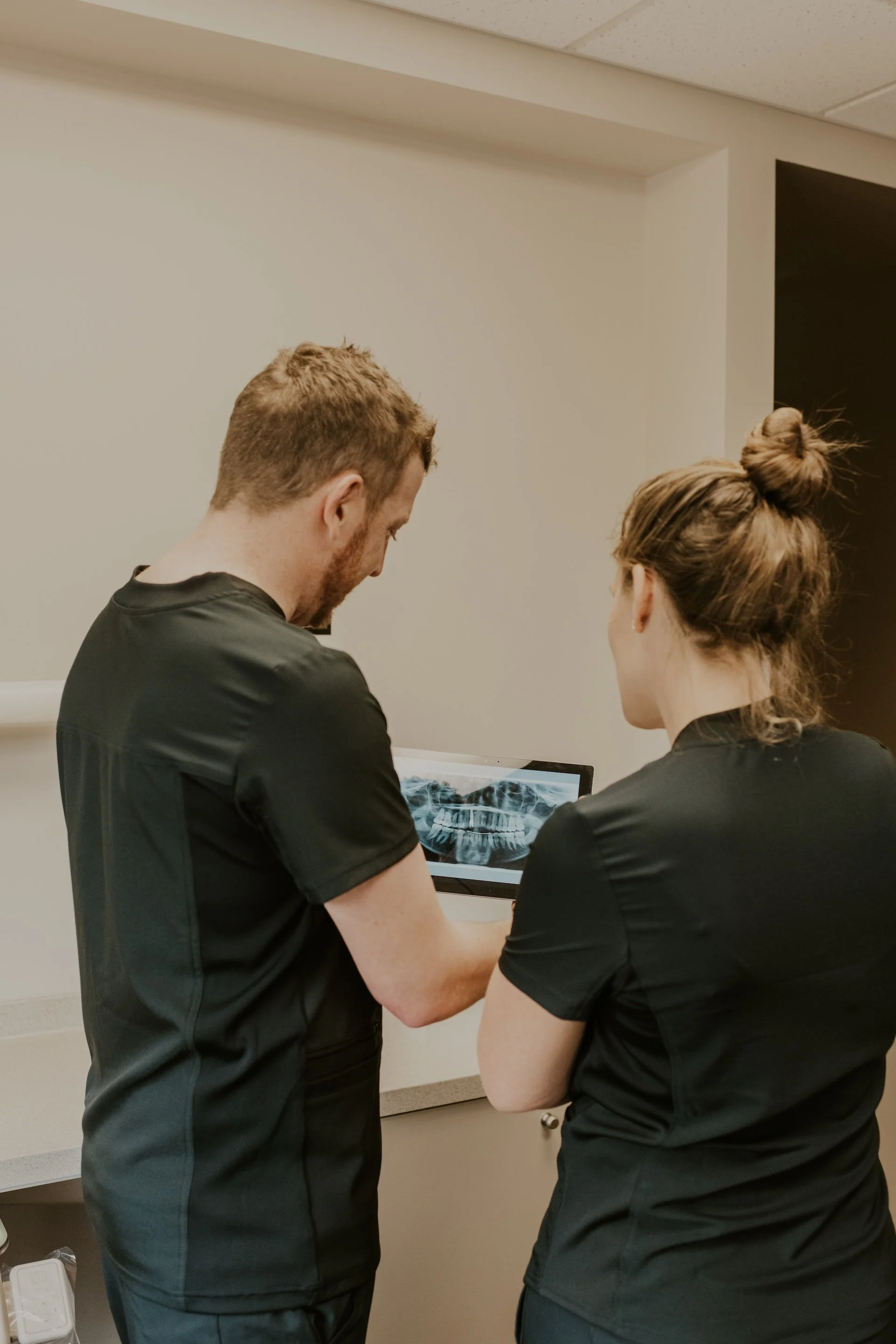 Two dental professionals examining a dental X-ray on a computer screen.