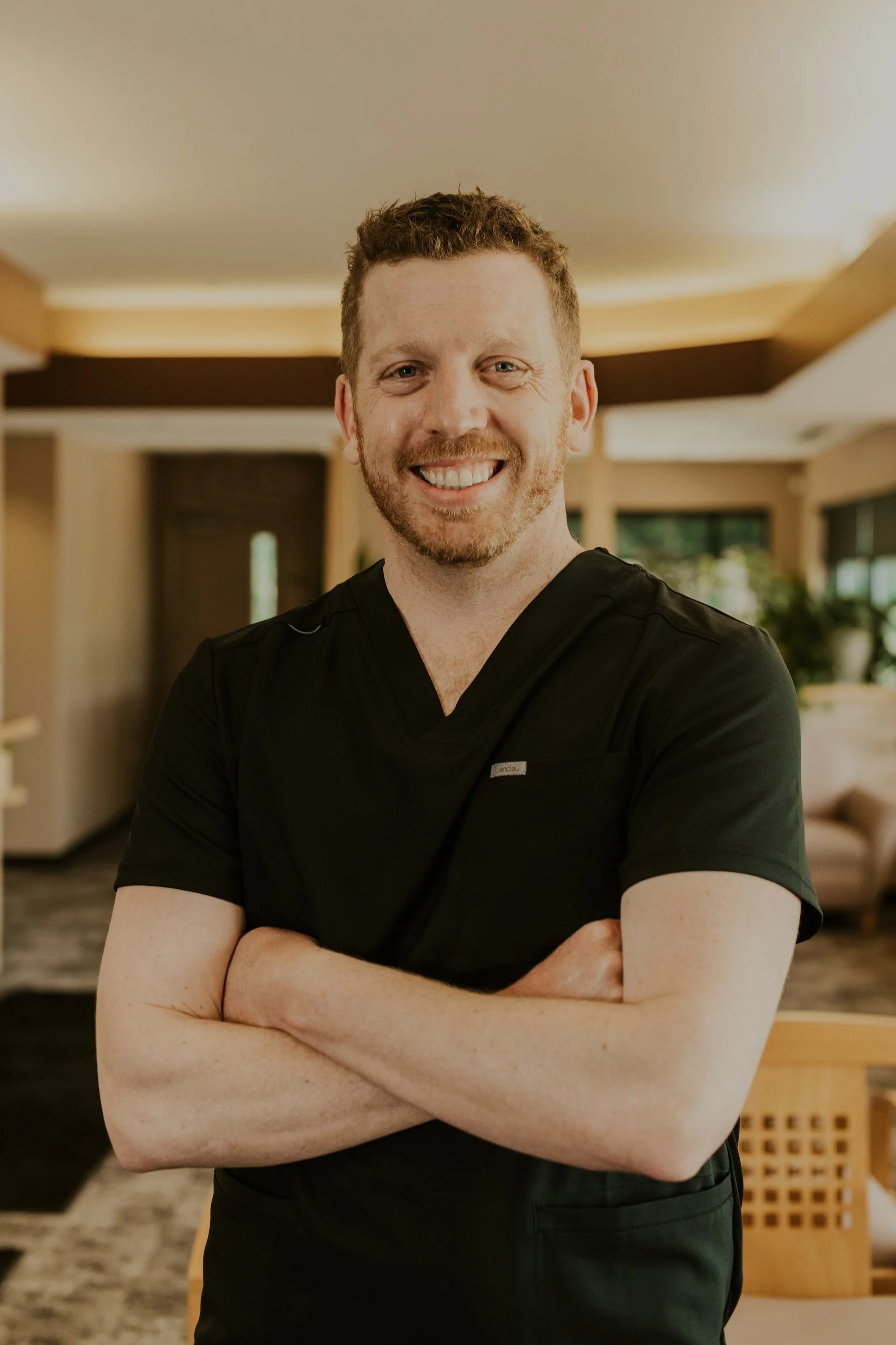 Dr. Matt Schneider smiling while wearing black scrubs and standing in the warmly lit Lakeville Family Dental office.