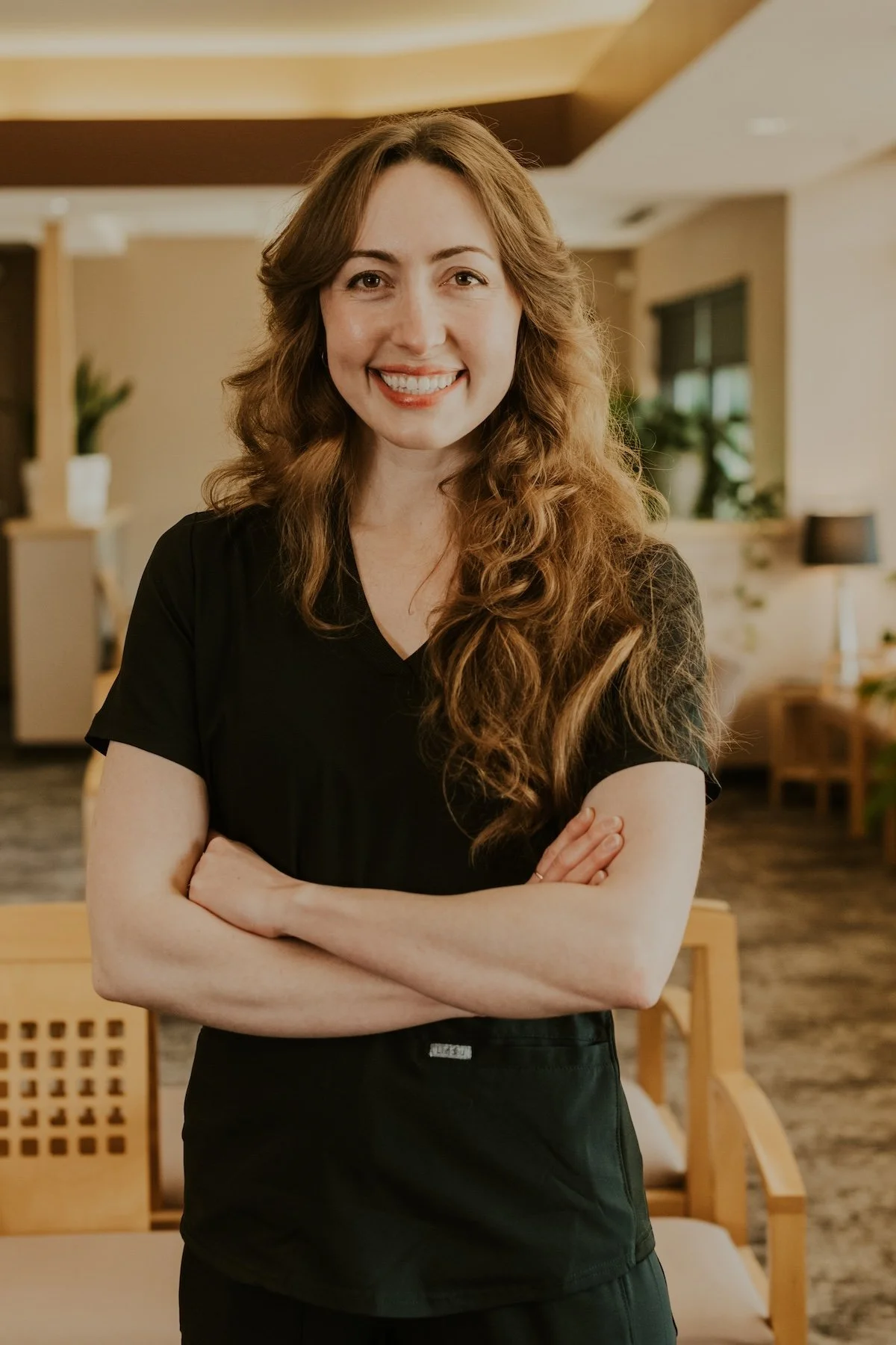 Dr. Riley Schulz smiling while wearing black scrubs and standing in the warmly lit Lakeville Family Dental office.
