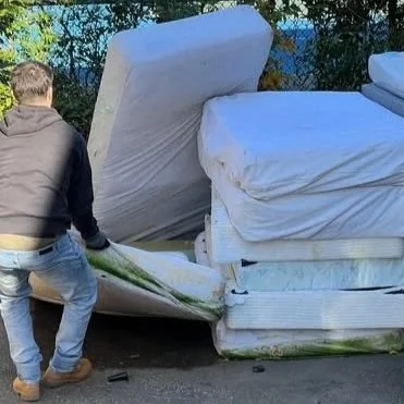 Person in black and gray hoodie moving a mattress outdoors.