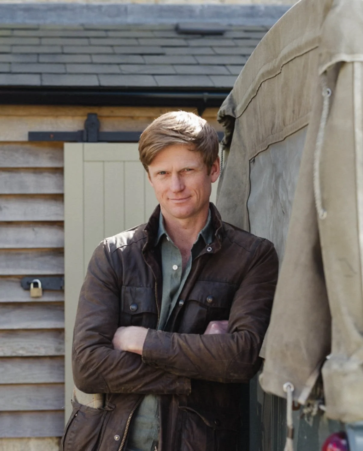 Ed Hall of Greenwild standing with arms crossed outside a wooden workshop next to a canvas covered Land Rover