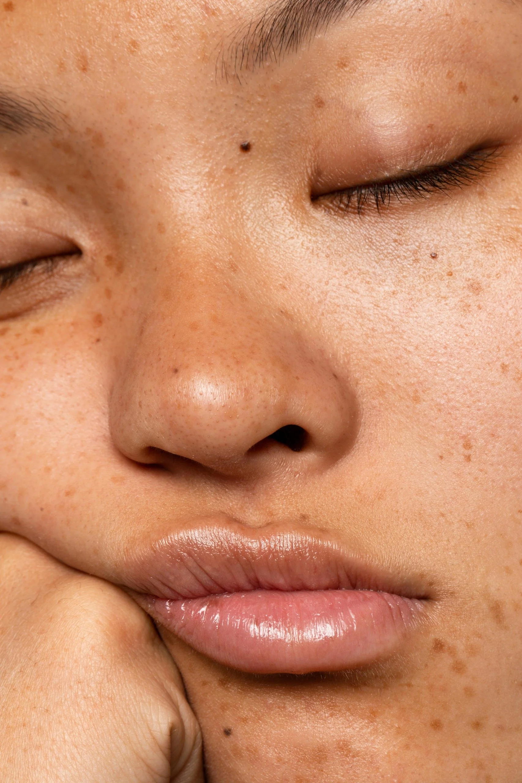 Close-up of a person's face focusing on the cheek, nose, lips, and closed eyes, showing detailed skin texture and freckles.