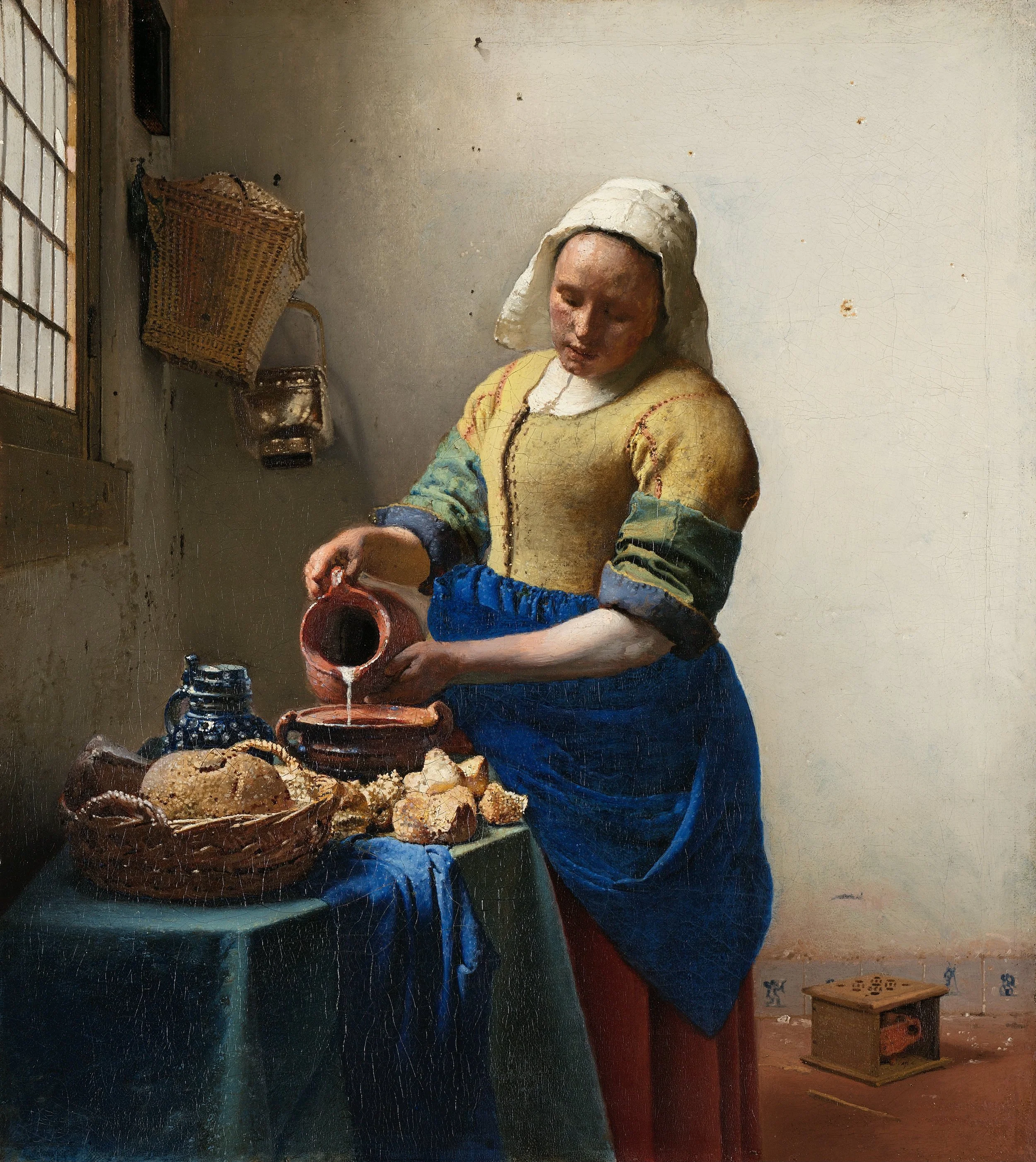 A woman in historical clothing pouring water into a bowl on a table with bread and pottery, in a simple interior with a window and wall accessories.